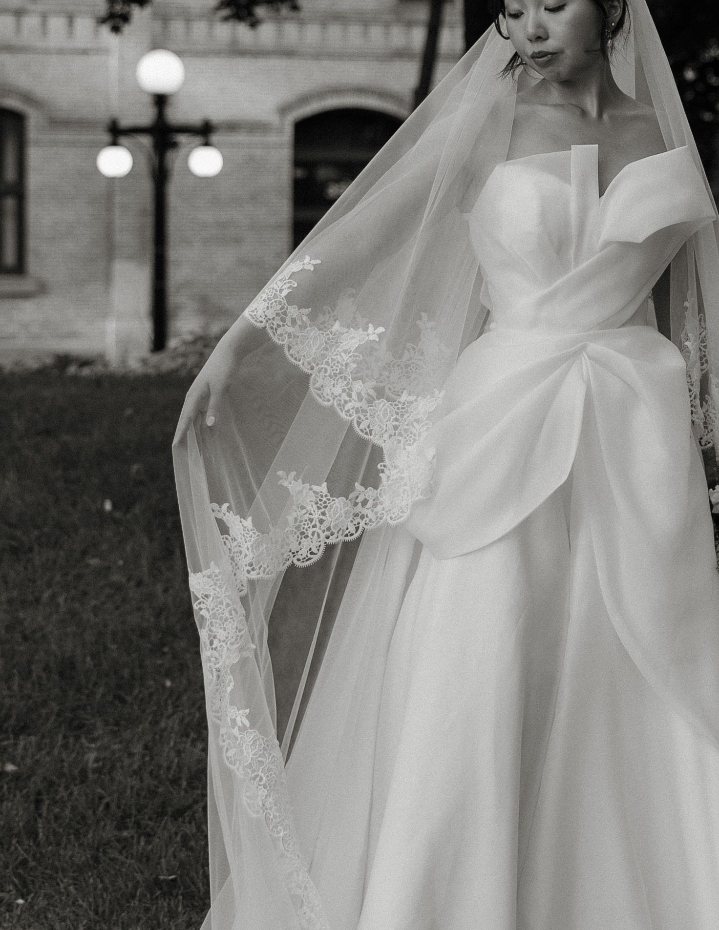 Black and white photo showing a flowing white wedding dress with delicate lace details and a long veil.