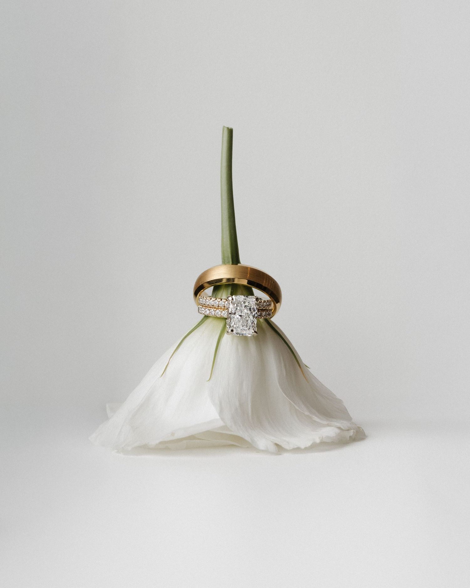 Two elegant wedding rings rest on a white tulip bud, featuring a gold band and diamond engagement ring.