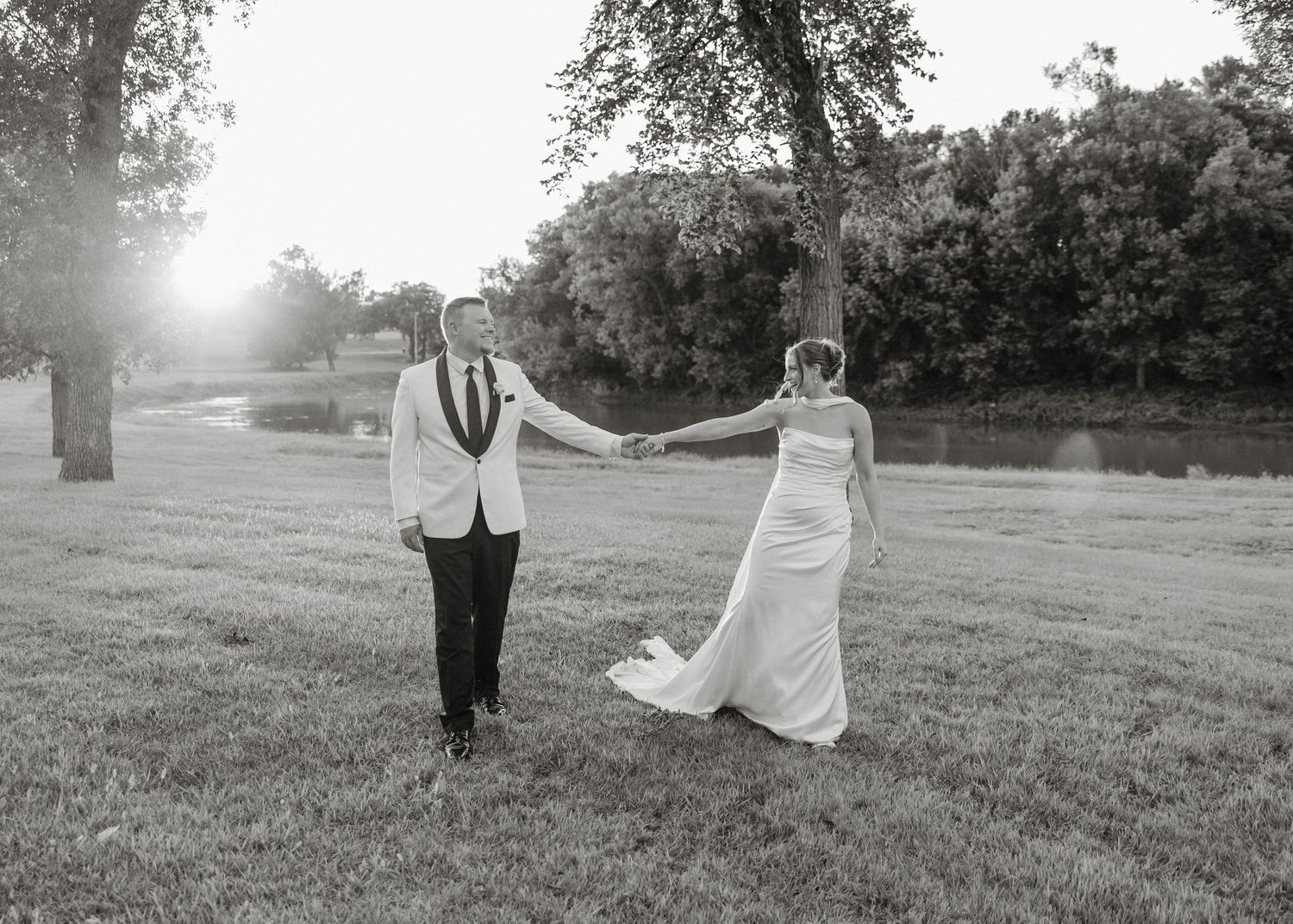 Black and white panoramic photo of a couple walking together in a sunlit meadow during golden hour.