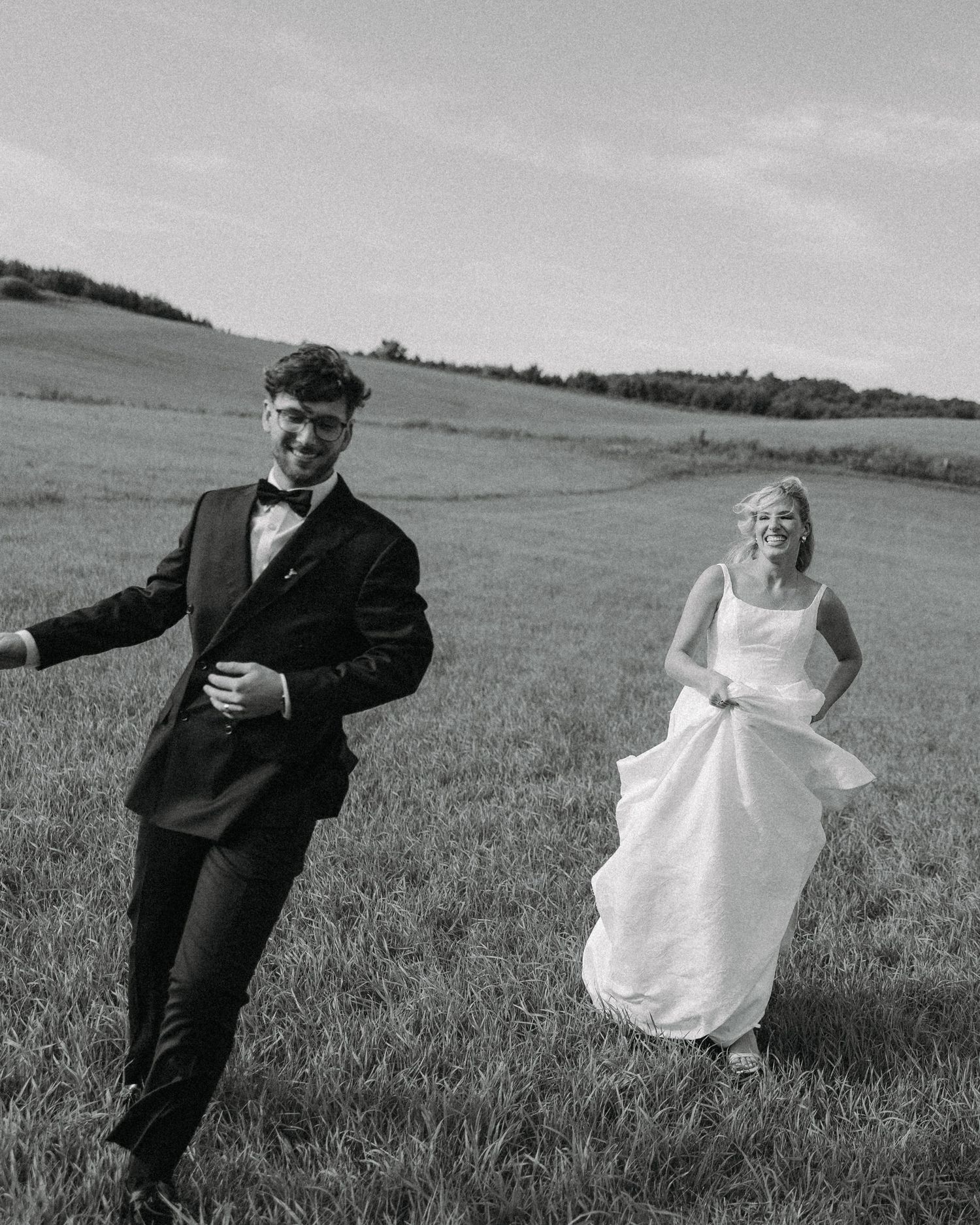 Black and white photo series showing a playful couple dancing and twirling in a countryside meadow.