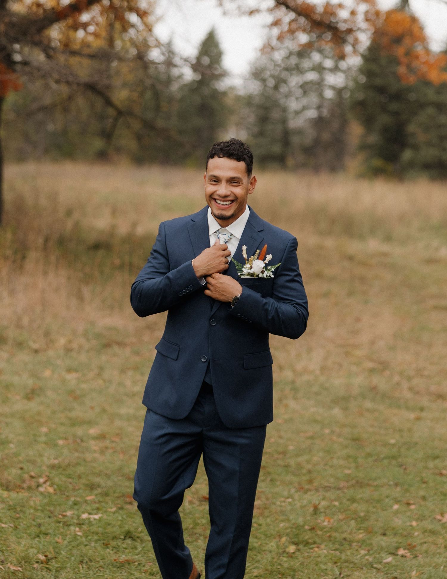 A person in a navy blue suit strikes playful poses in a field during autumn.