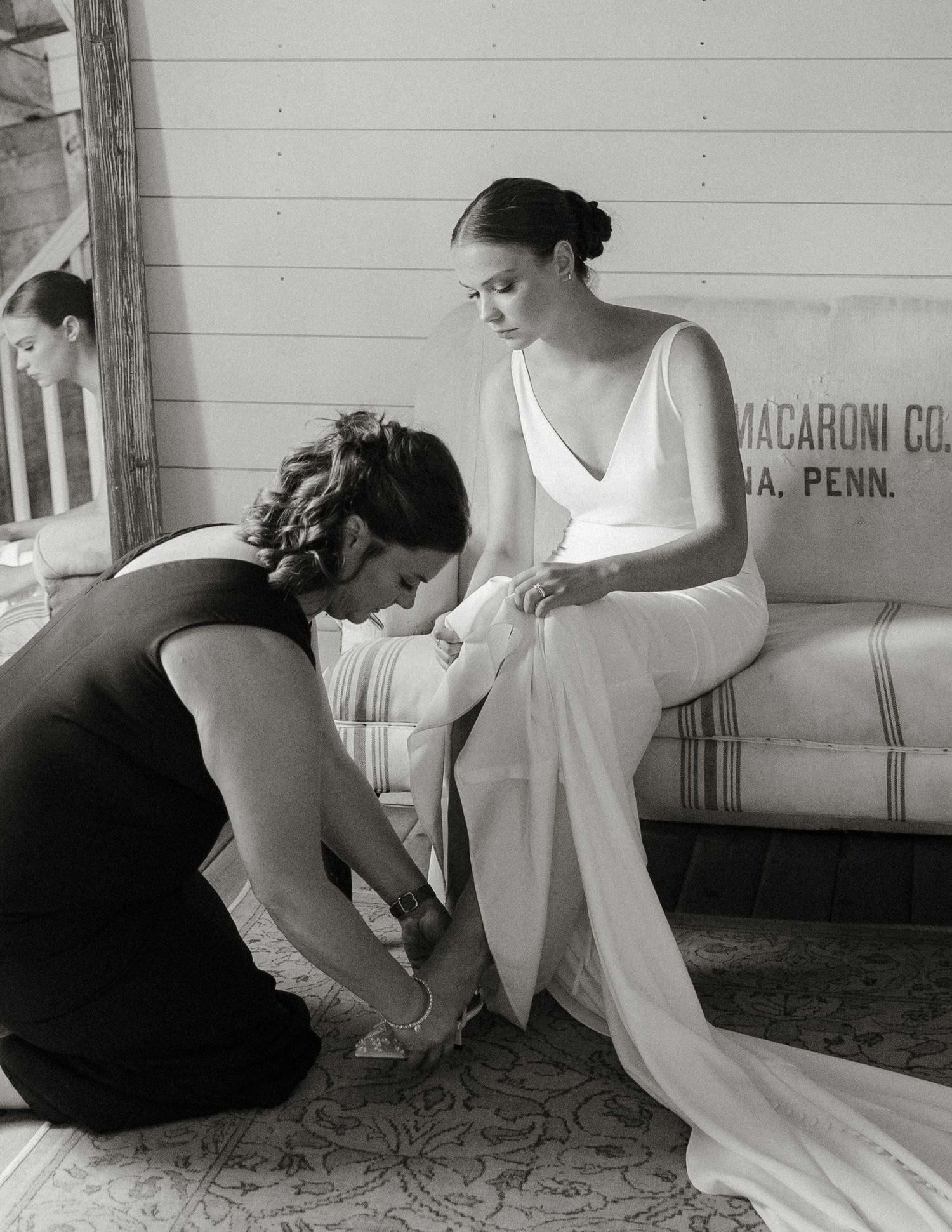 Black and white photo of a bridesmaid helping a bride with her shoes before the wedding ceremony.