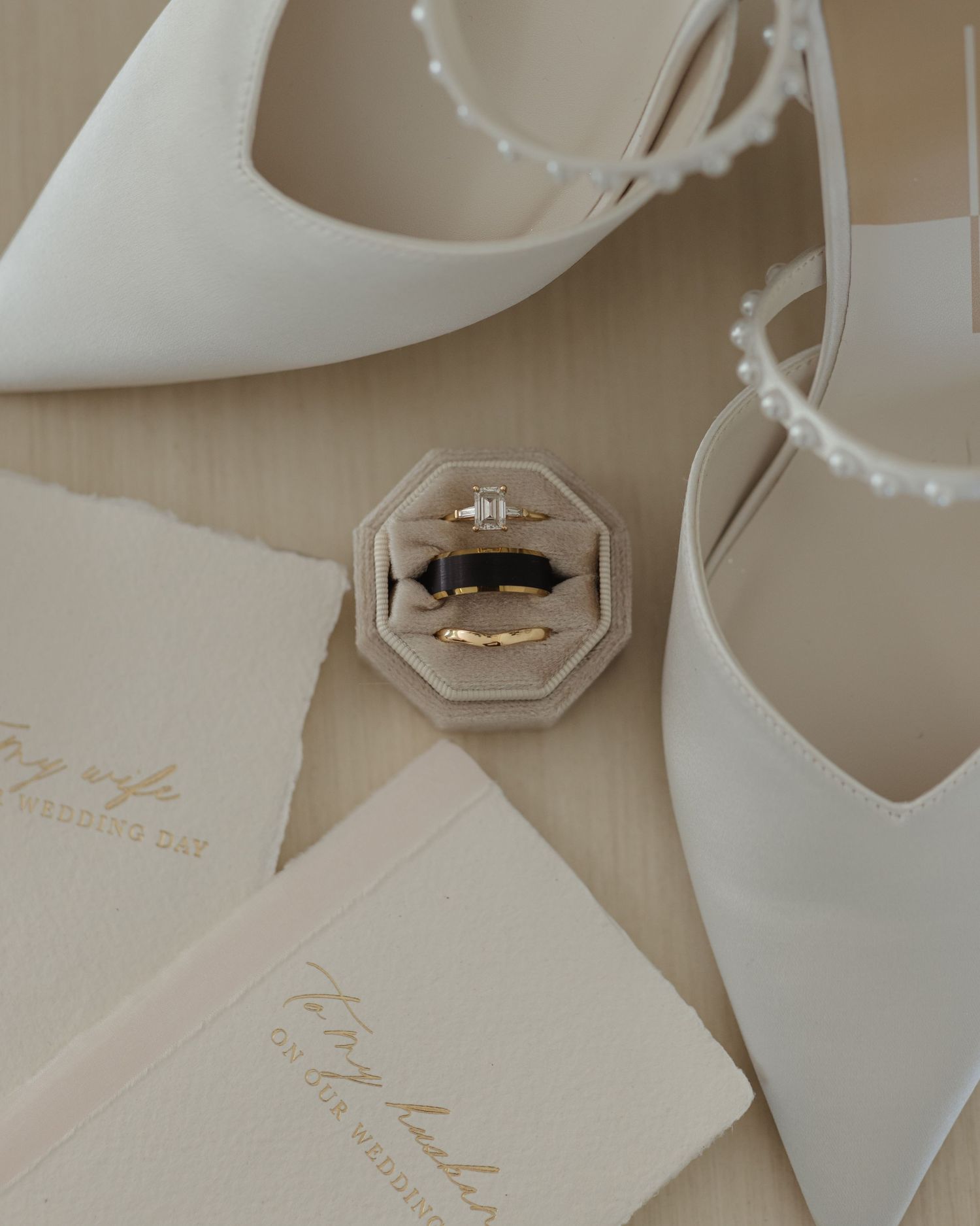Wedding details including white bridal shoes, delicate name cards, and a diamond engagement ring on a neutral surface.
