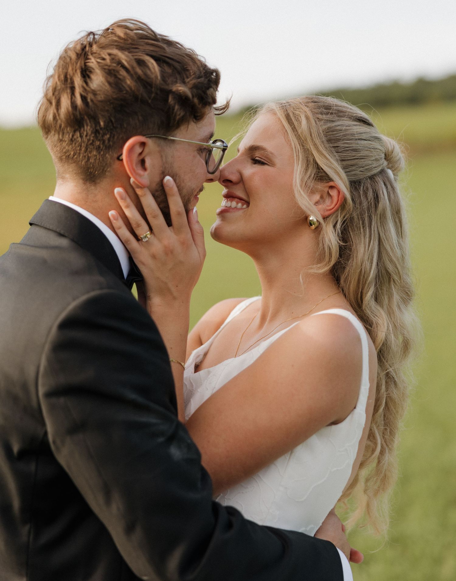 A romantic wedding photo of a couple sharing an intimate moment outdoors in a field.