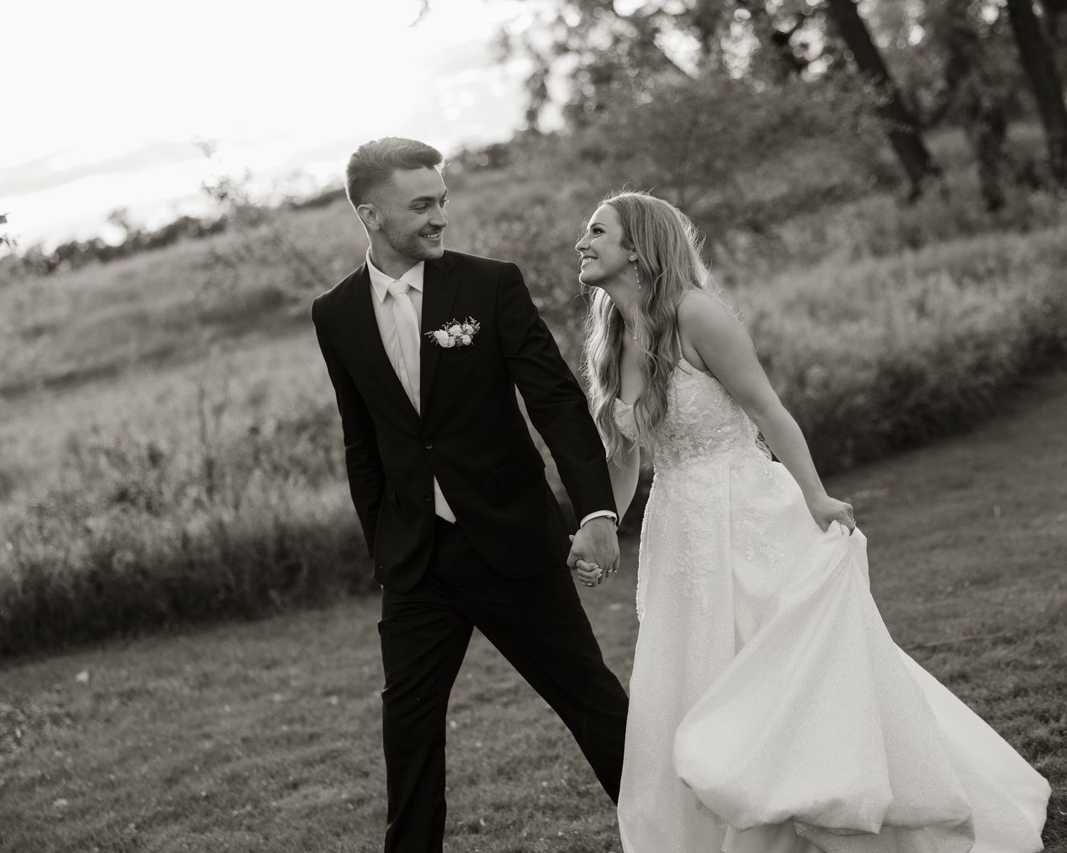 A joyful couple in wedding attire playfully runs through a scenic field during their outdoor photo session.