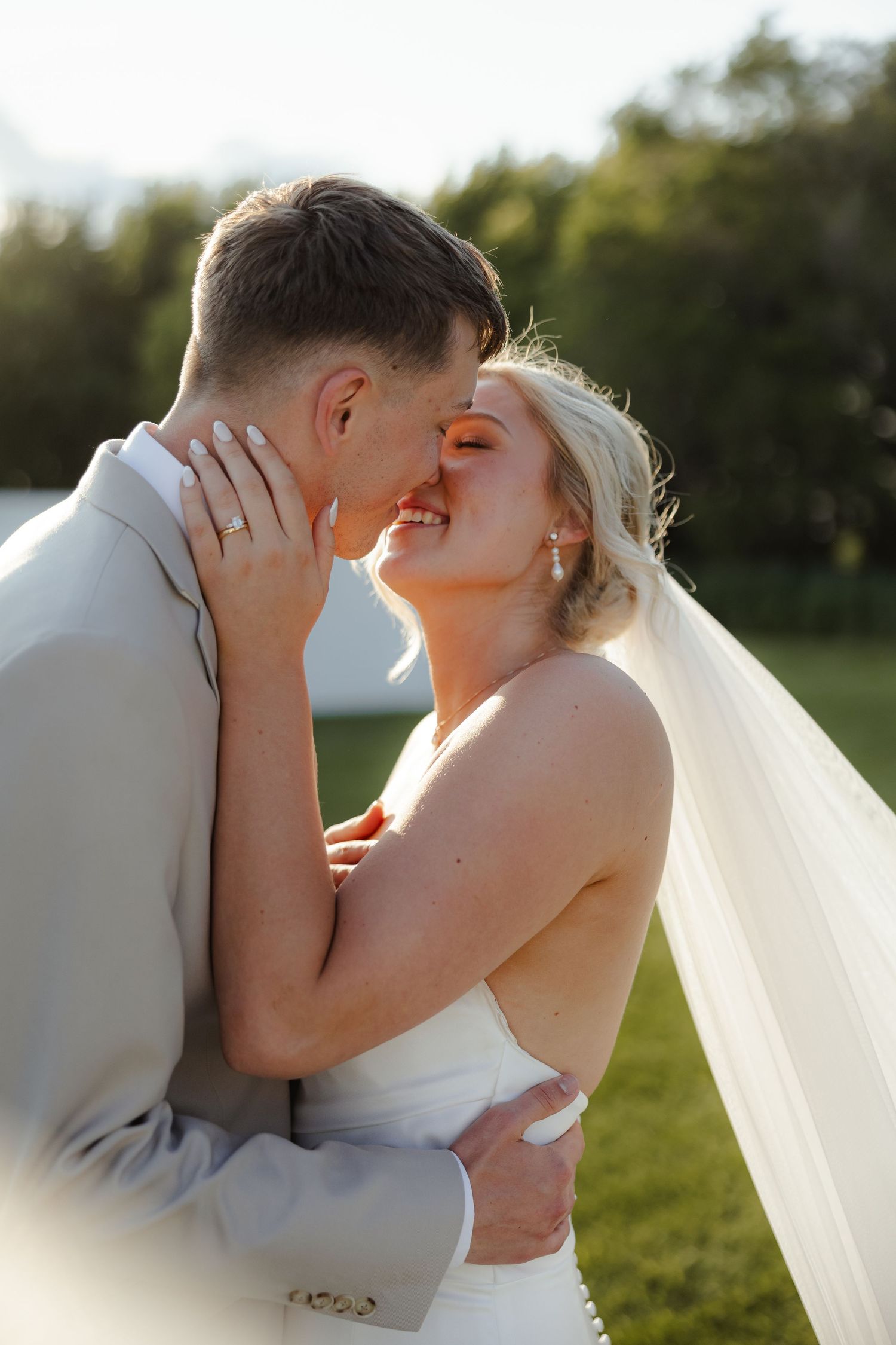A romantic wedding moment captured at sunset with a couple sharing an intimate kiss in an outdoor setting.