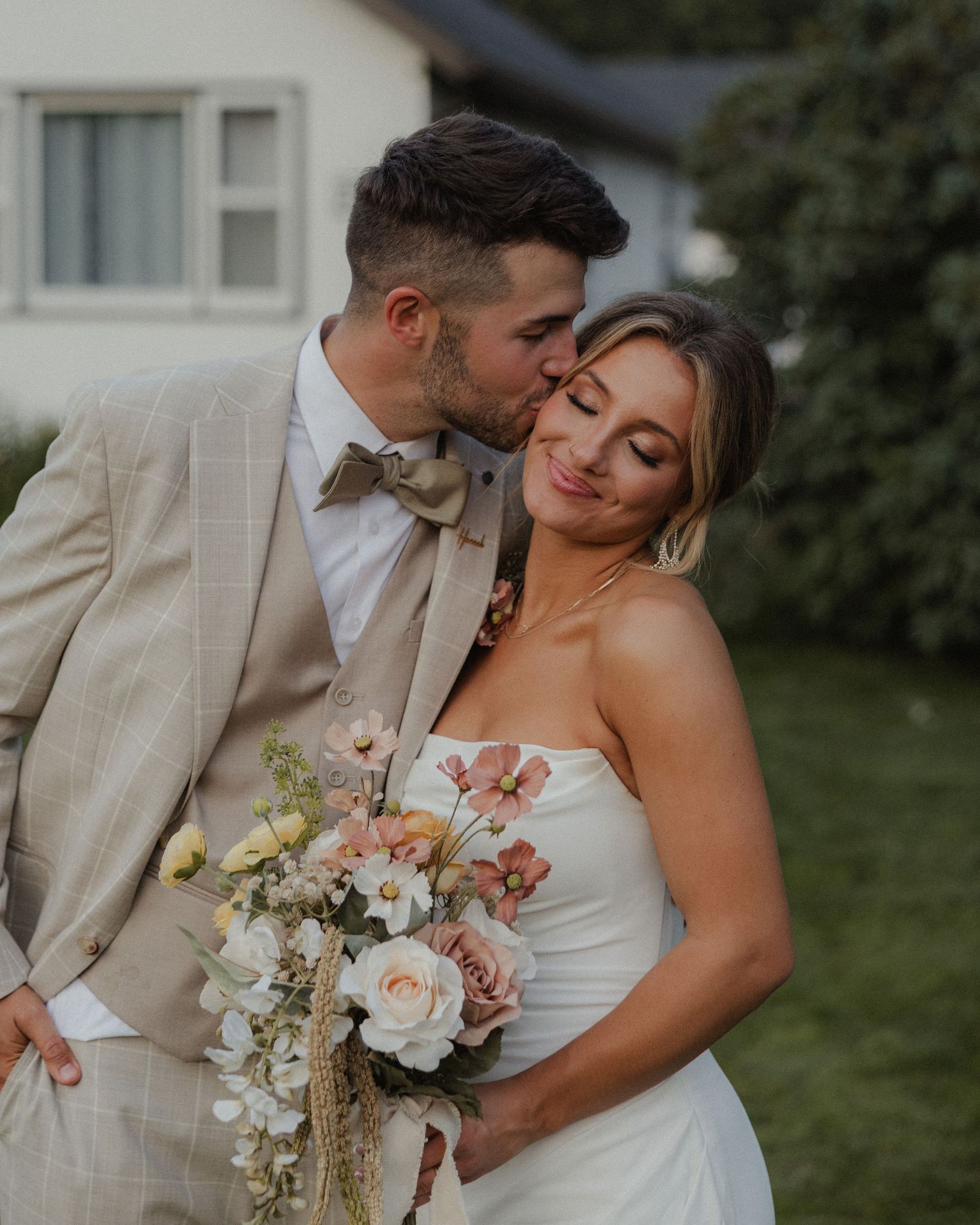 Wedding couple embracing in formal attire with floral bouquet.