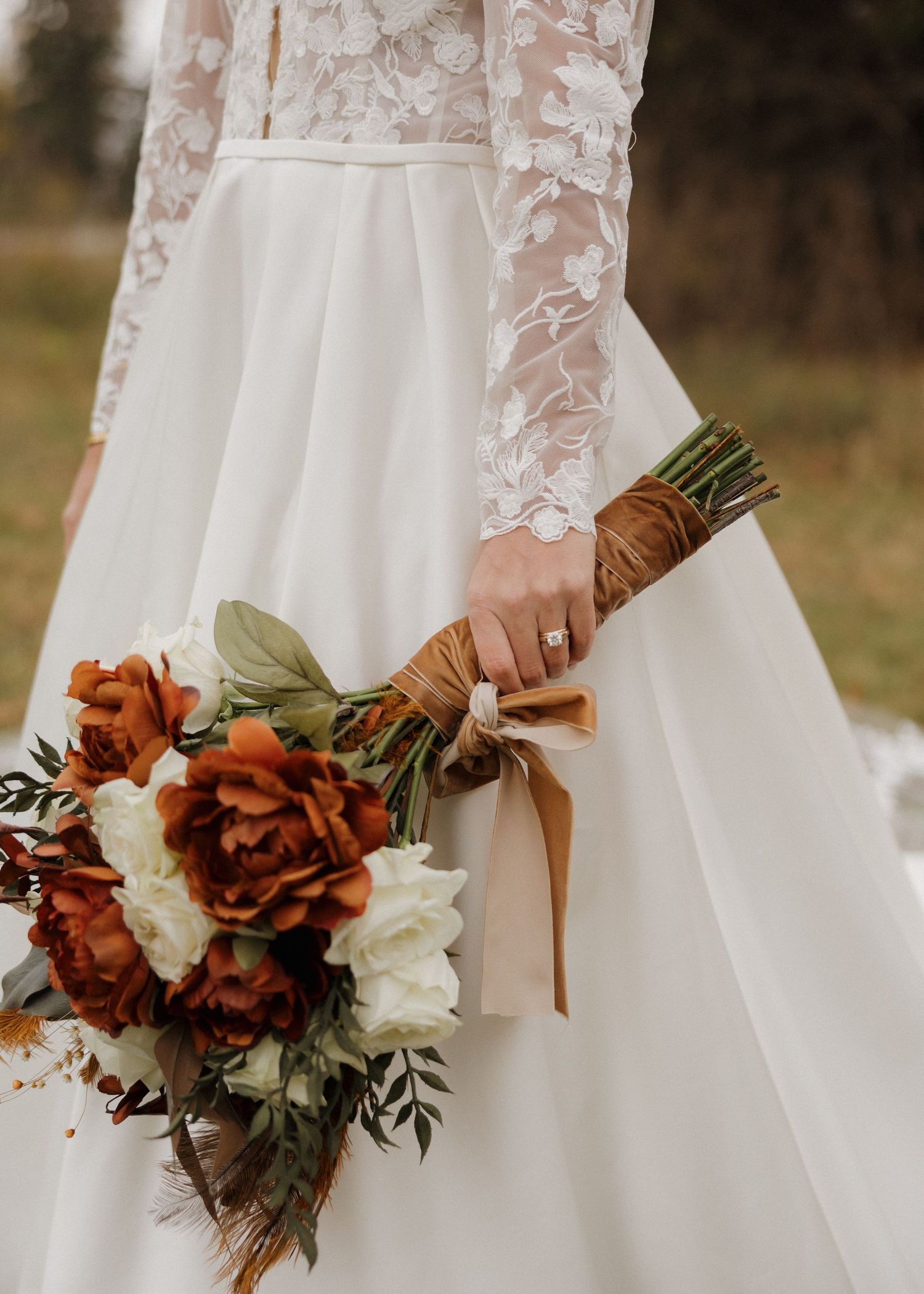 A row of white wedding dresses with autumn-themed bouquets featuring rust-colored roses and greenery.