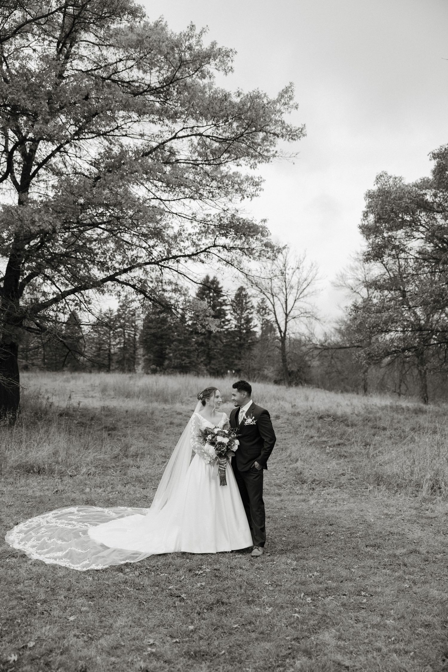 A romantic black and white wedding photoshoot sequence showing a couple in a meadow with tall trees in the background.