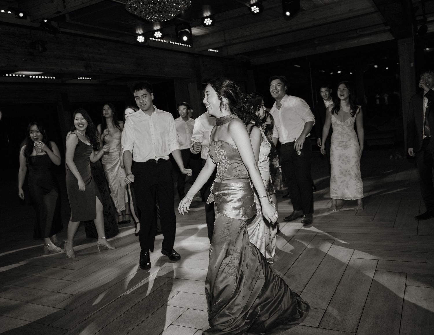 Black and white photo of wedding guests dancing and celebrating at an indoor reception venue.