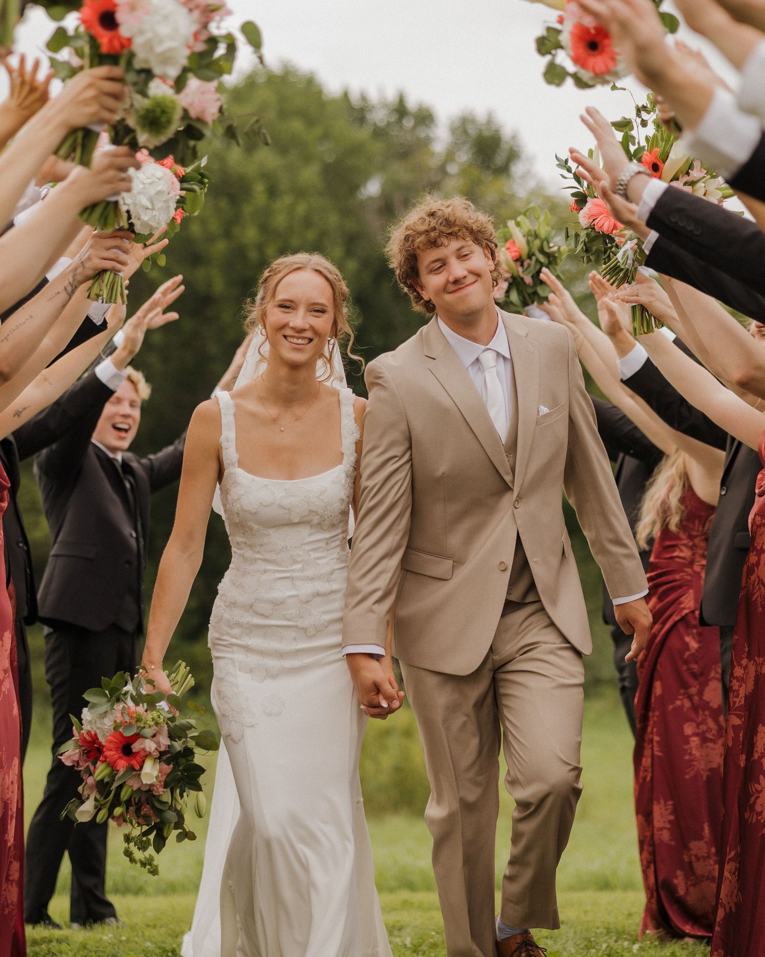 Wedding party celebrates outdoors with raised hands and floral bouquets in a joyful moment.