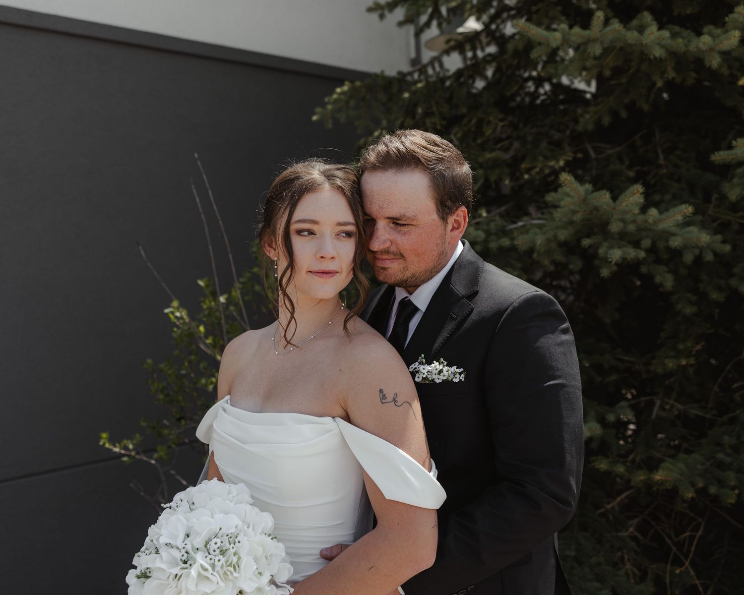 Elegant wedding couple embraces in romantic outdoor garden setting with lush greenery backdrop.