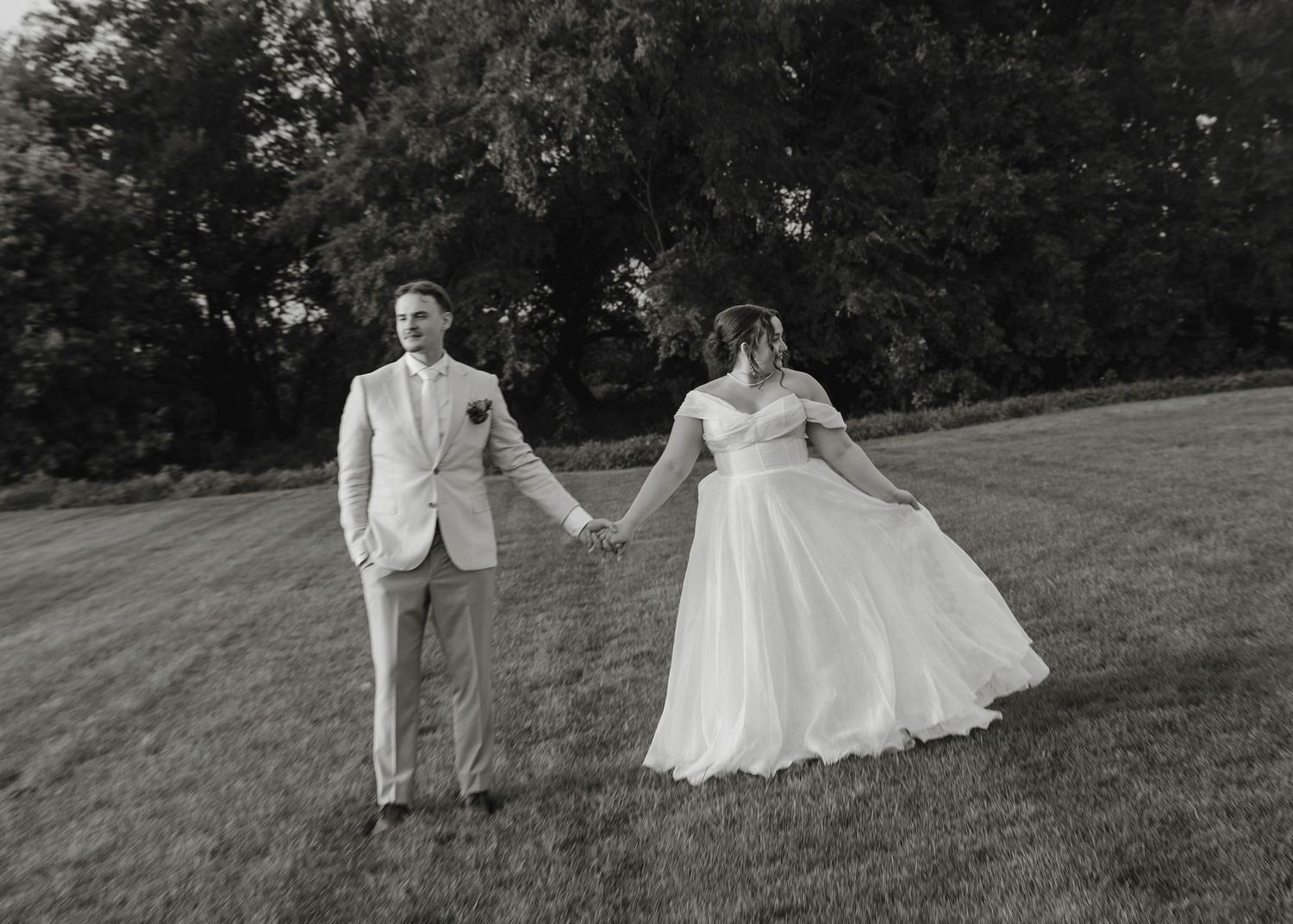 Black and white wedding photos show a couple joyfully running and dancing together on a grassy hillside.