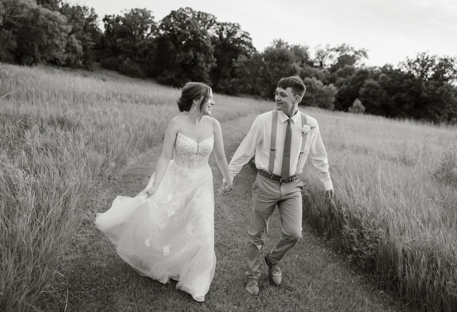 A couple walks hand in hand through a scenic meadow with tall grass on a sunny summer day.