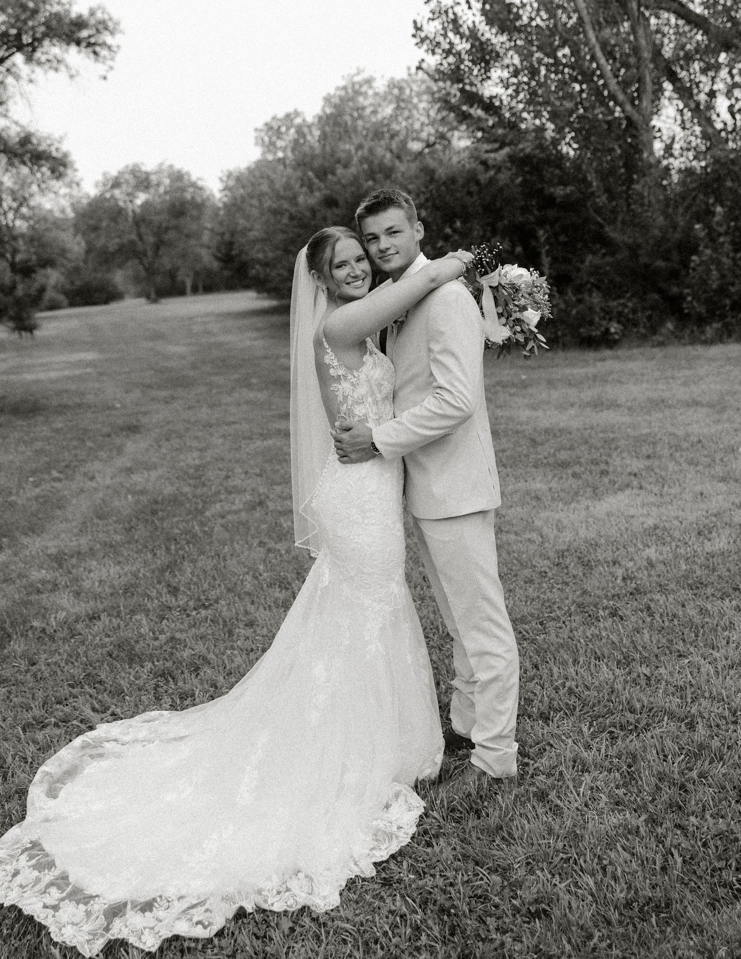 A romantic black and white wedding photo series showing a couple embracing on a grassy hillside in formal attire.
