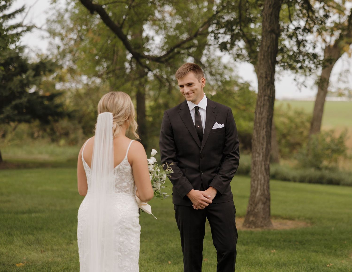 A first look wedding moment captured in a serene outdoor setting with trees and natural lighting.