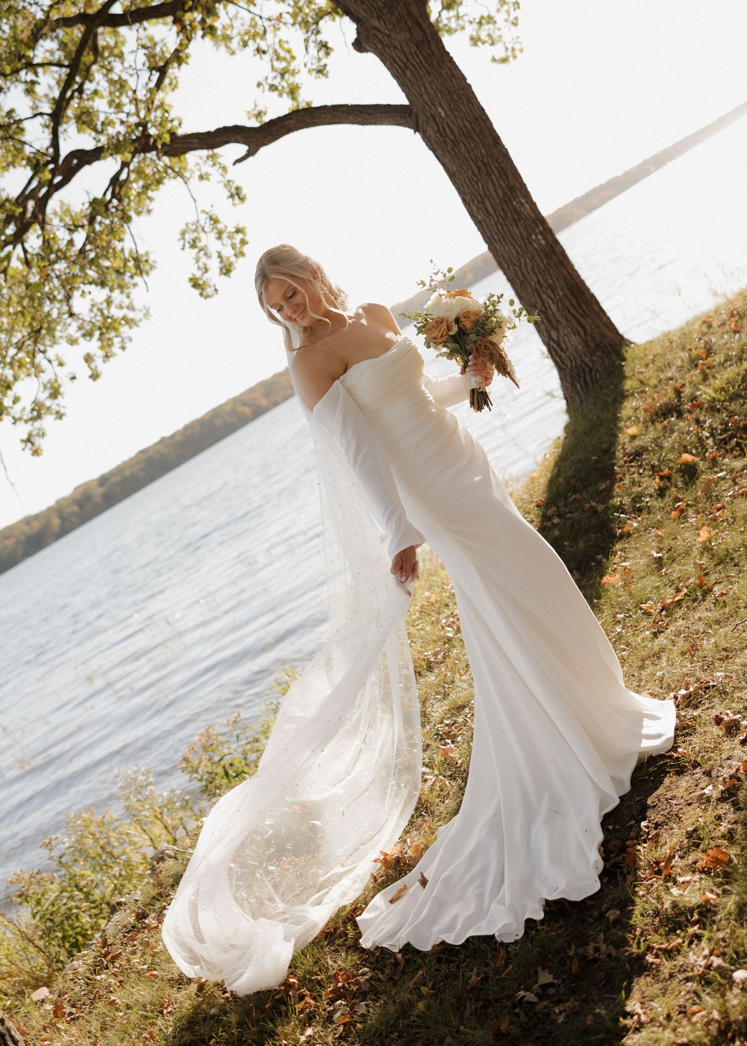 A bride in a flowing white dress twirls gracefully by a lakeside at sunset, creating a dreamy silhouette effect.