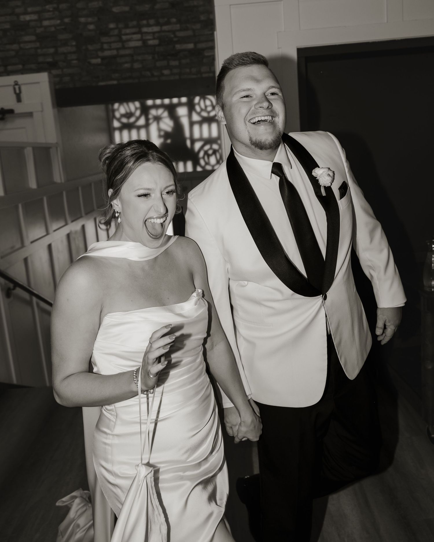 A happy couple laughs together at their wedding reception while wearing white formal attire.