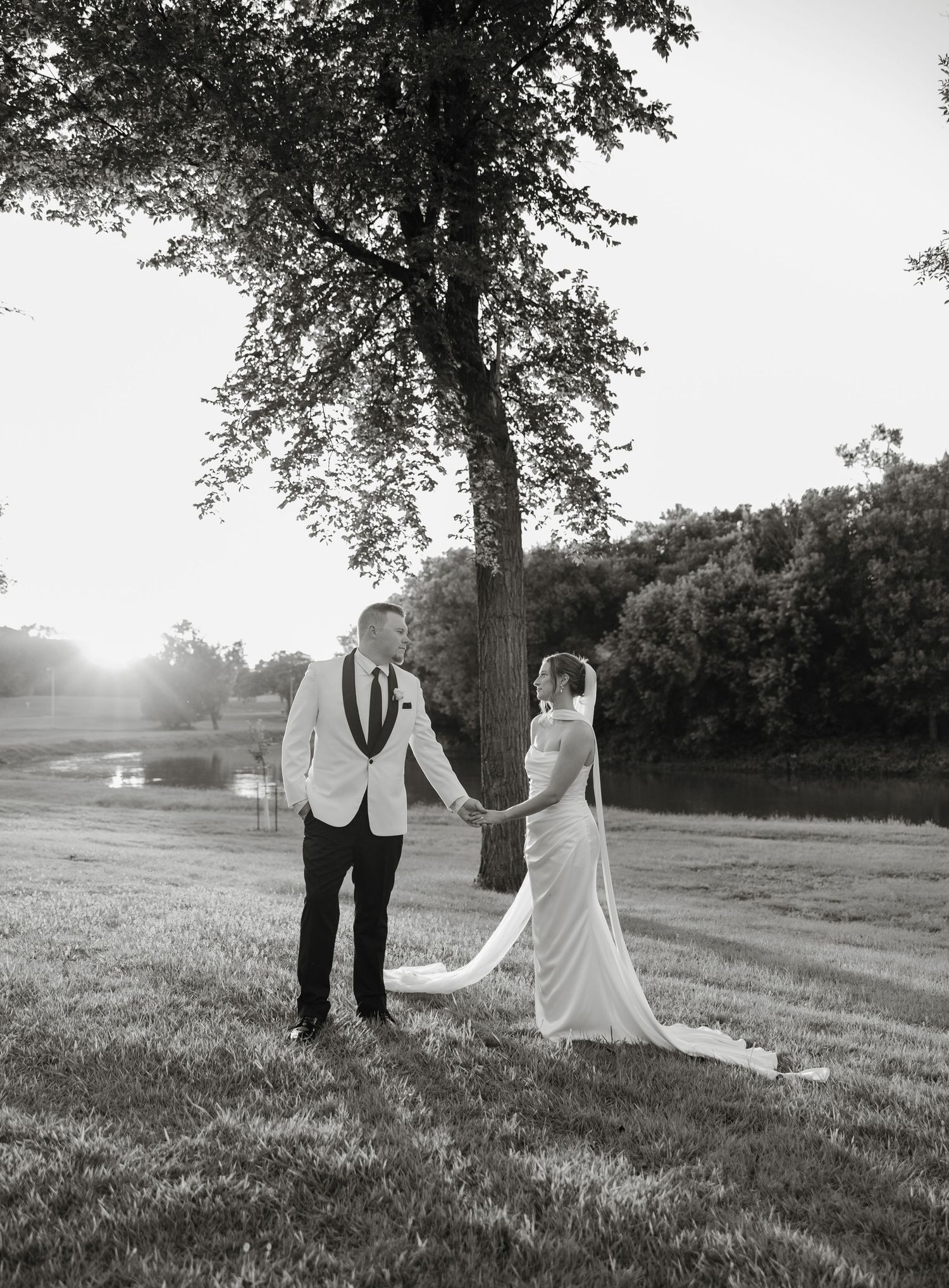 A couple shares an intimate moment at sunset in a grassy field beneath a large tree.