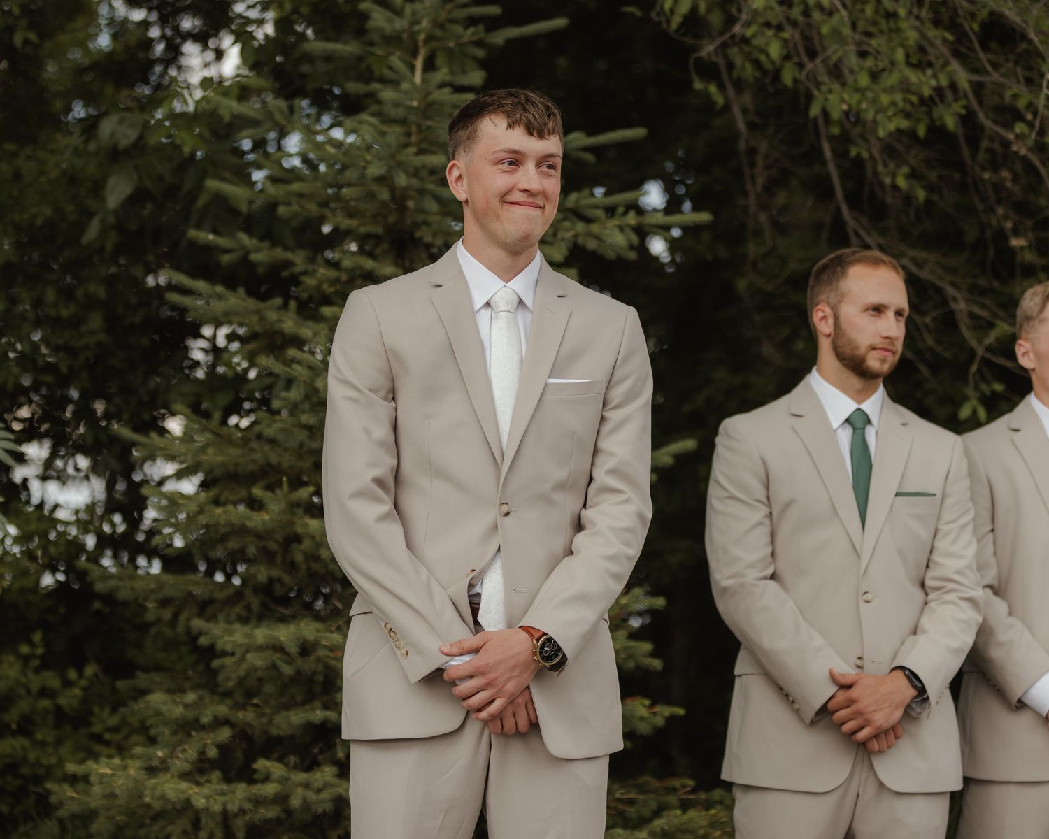 Groomsmen in light tan suits and colorful ties standing together outdoors.