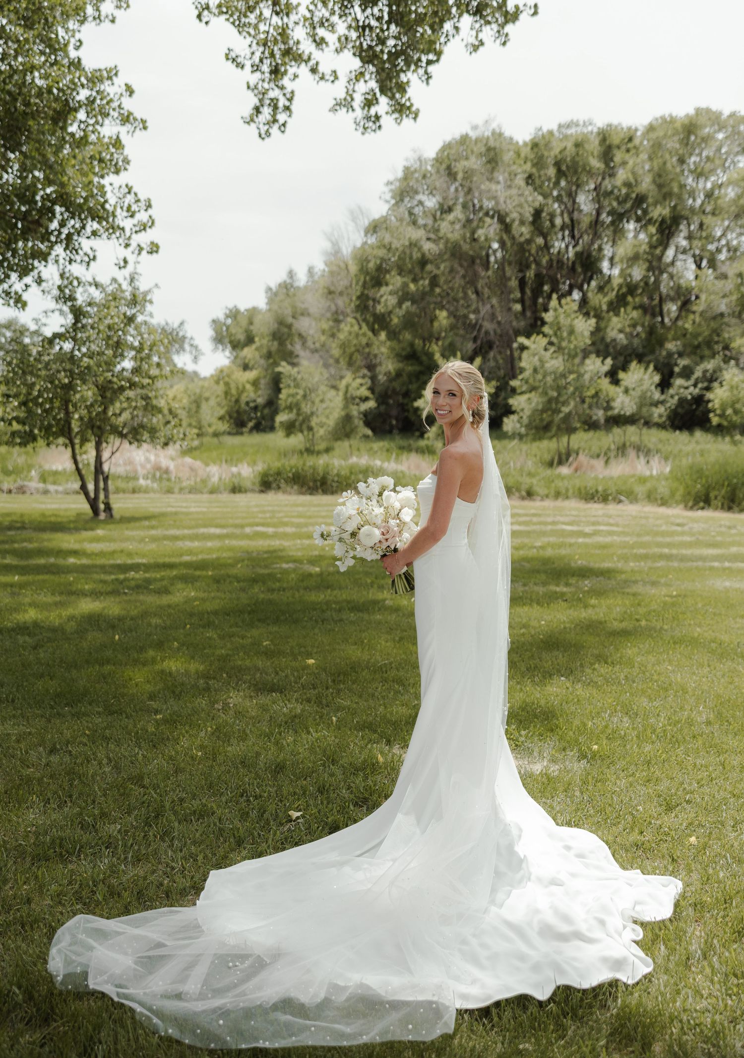 A bride in a flowing white gown poses with her bouquet in a lush garden setting.