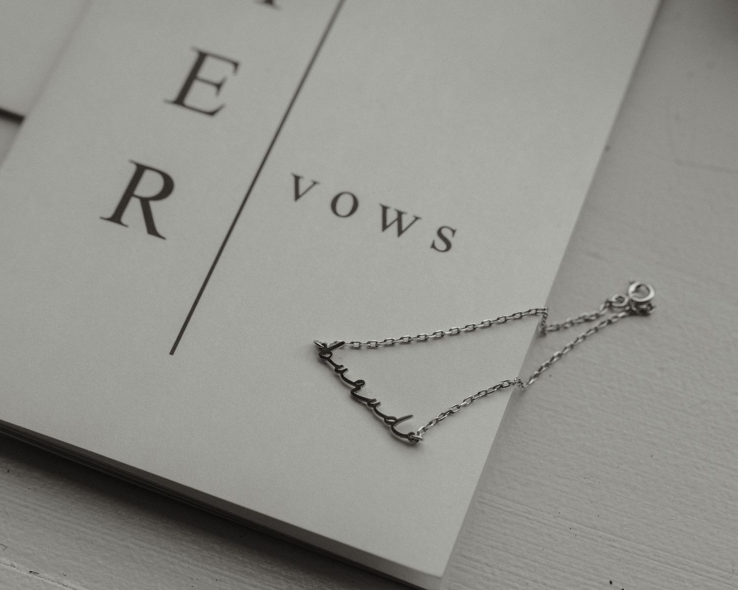 A delicate silver chain necklace rests on a book with text 'vows' visible.
