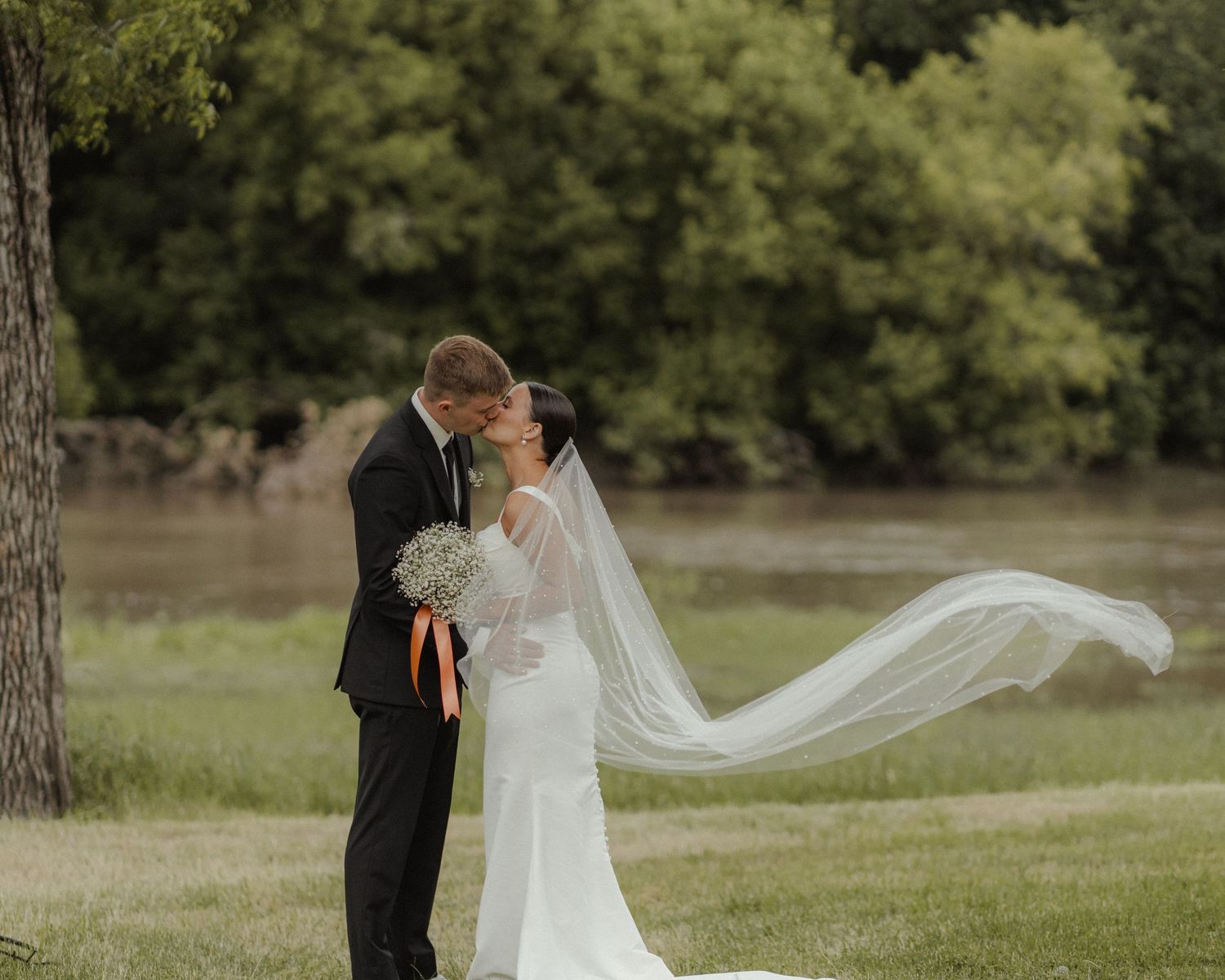 Wedding couple enjoying a romantic moment outdoors with a flowing white veil.