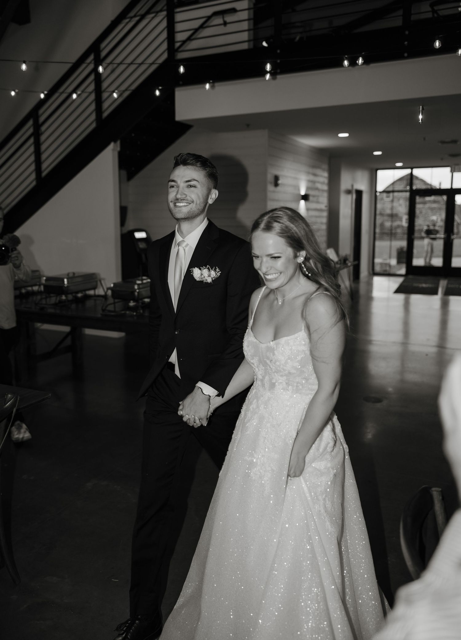Black and white wedding photo sequence showing happy couple walking and laughing together in a modern indoor venue.