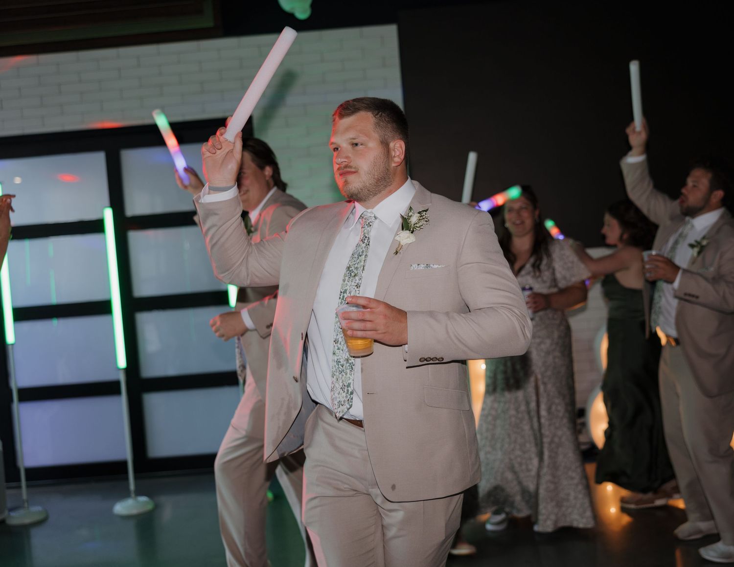 Wedding guests dancing and celebrating at a reception with hands raised in the air.