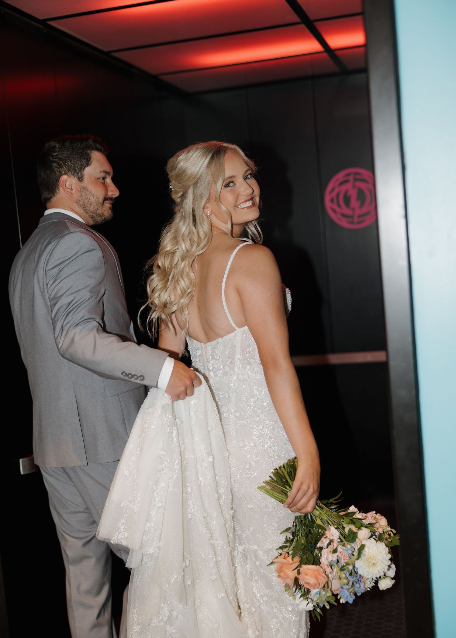 A couple in wedding attire shares a romantic moment in a dimly lit venue with red and blue lighting.