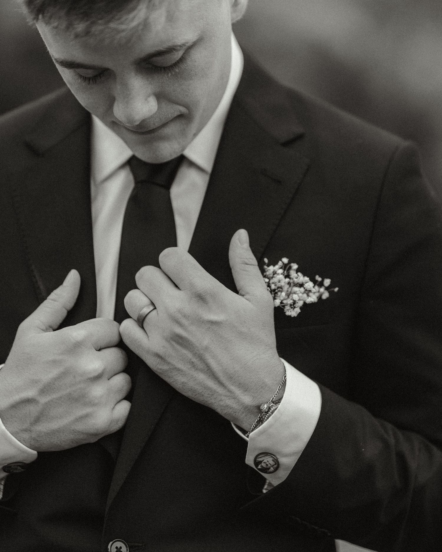 Elegant black and white photo of groom adjusting suit with boutonniere.
