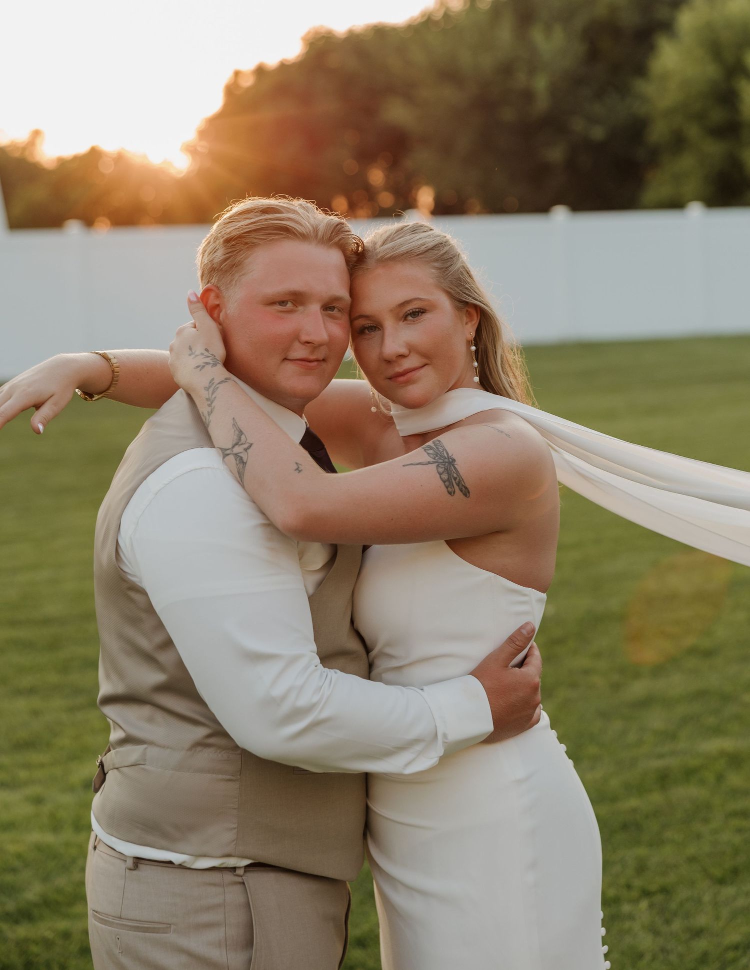A romantic sunset wedding portrait of a couple embracing outdoors with warm golden light and flowing dress details.