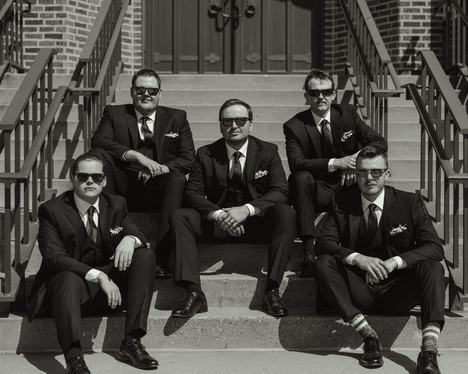 A sequence of black and white photographs showing people sitting on steps wearing suits and dark sunglasses.