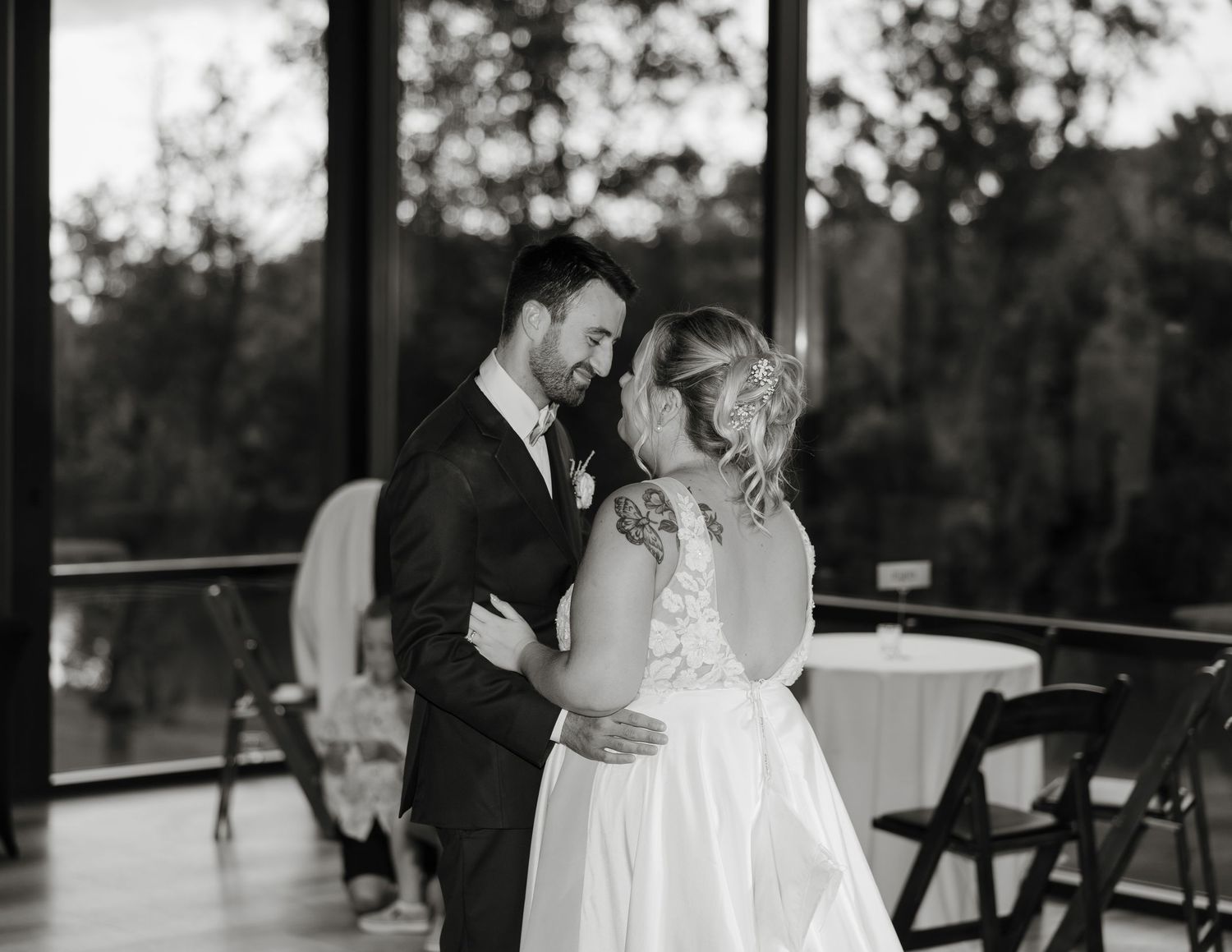 A couple shares their first dance together in a romantic black and white moment at an indoor wedding venue.