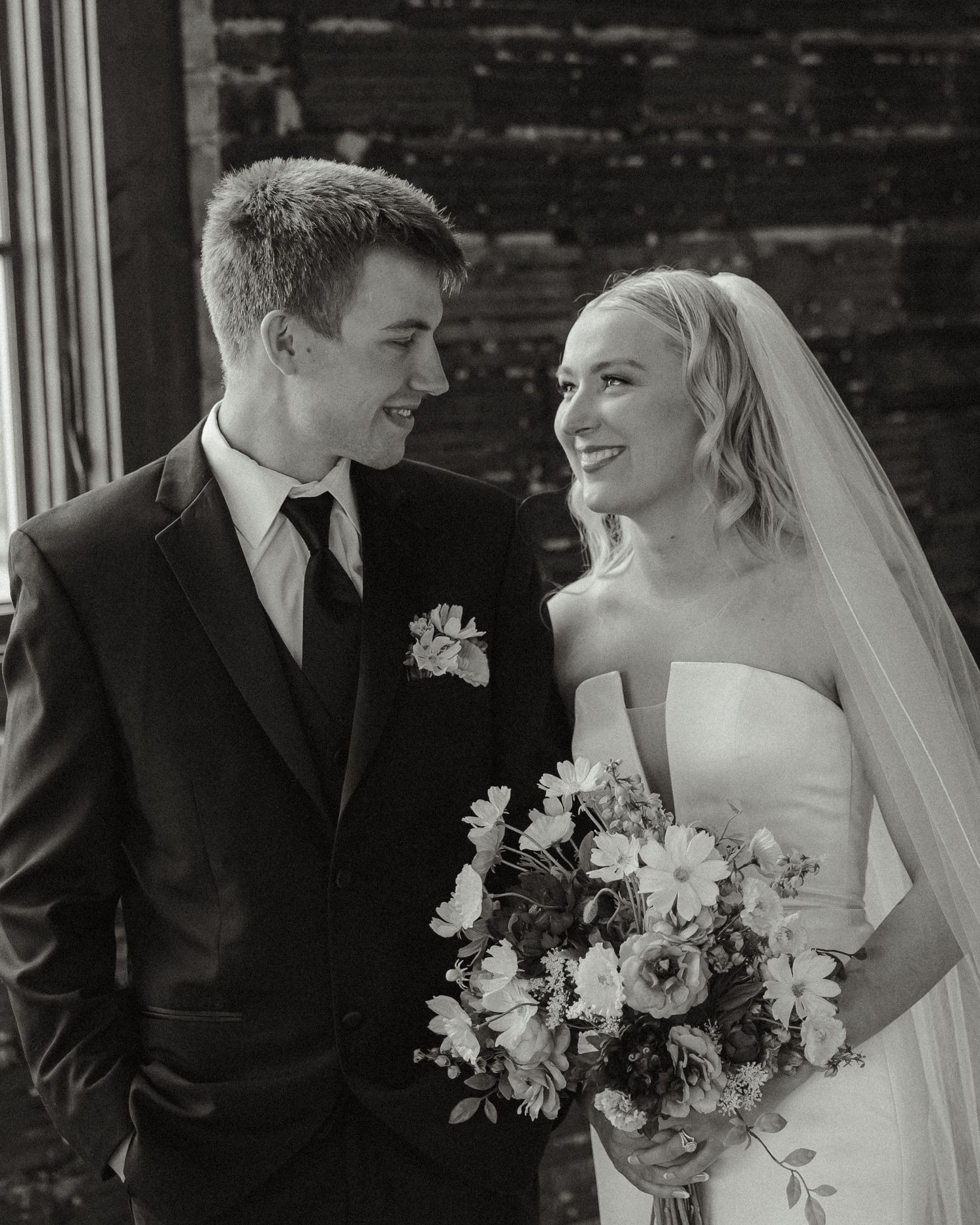 Black and white wedding portraits with elegant floral bouquet against rustic backdrop.