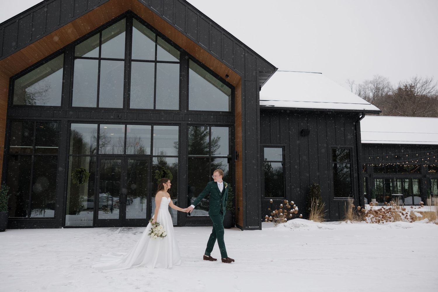 Modern black barn-style wedding venue exterior with large windows and snowy landscape in winter.