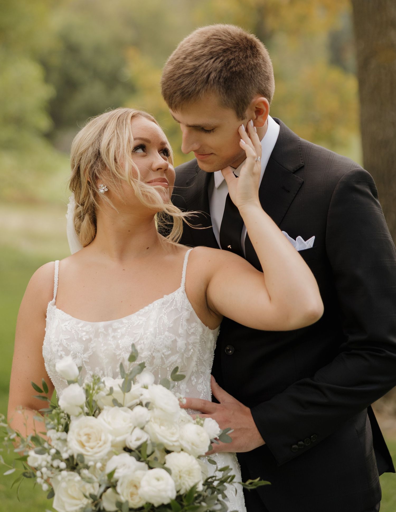 A romantic wedding couple shares intimate moments in an autumn outdoor setting with white floral bouquets.