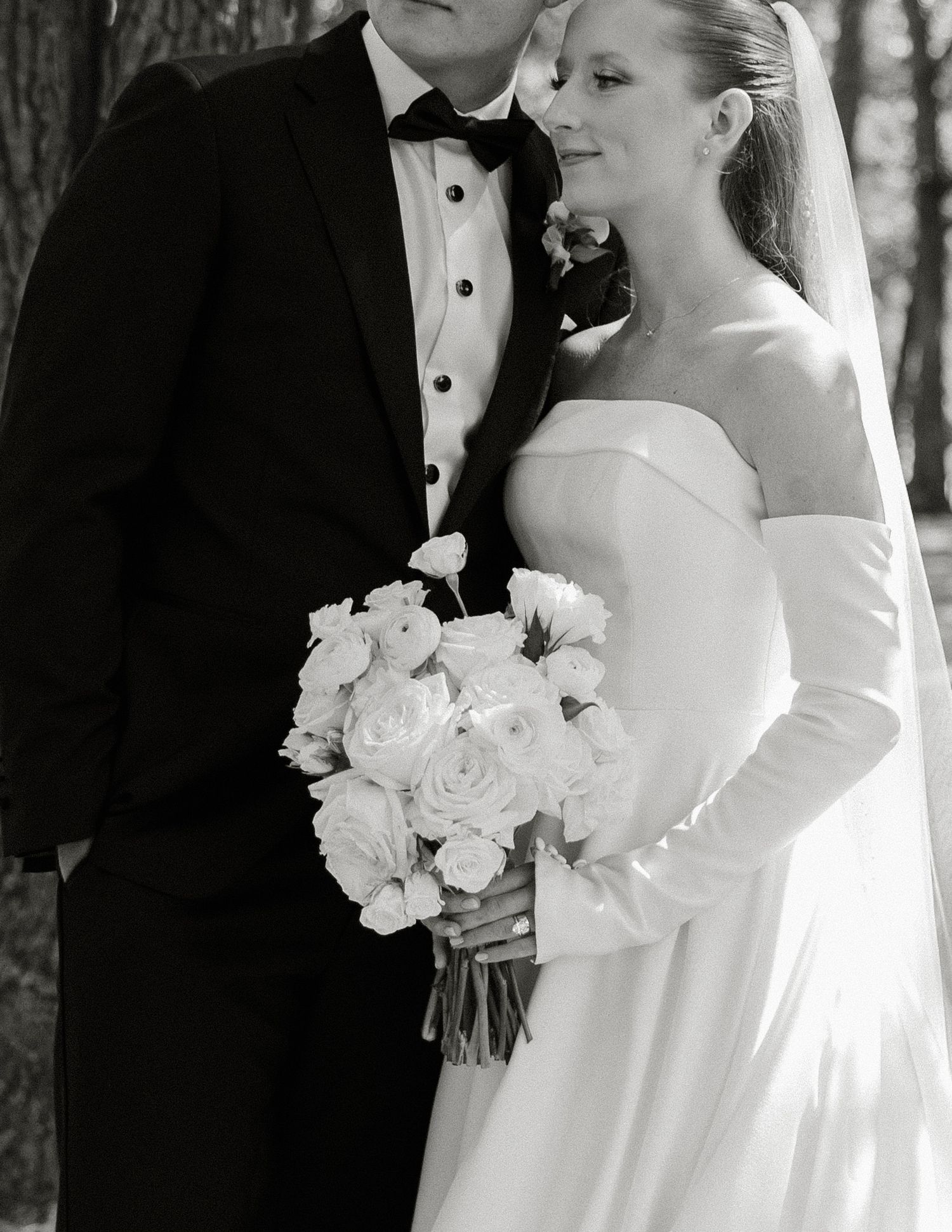 Black and white wedding photo showing couple in formal attire with bride holding white rose bouquet.