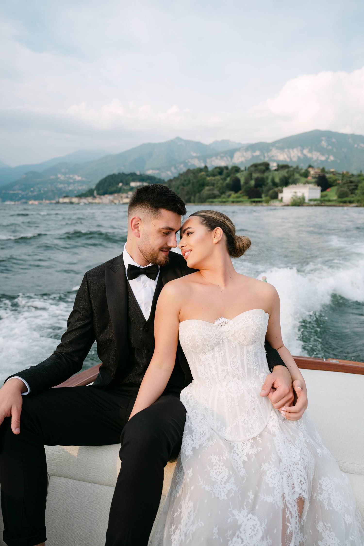 Bride and groom share a romantic moment on a luxury yacht with Italian lake mountains in the background.