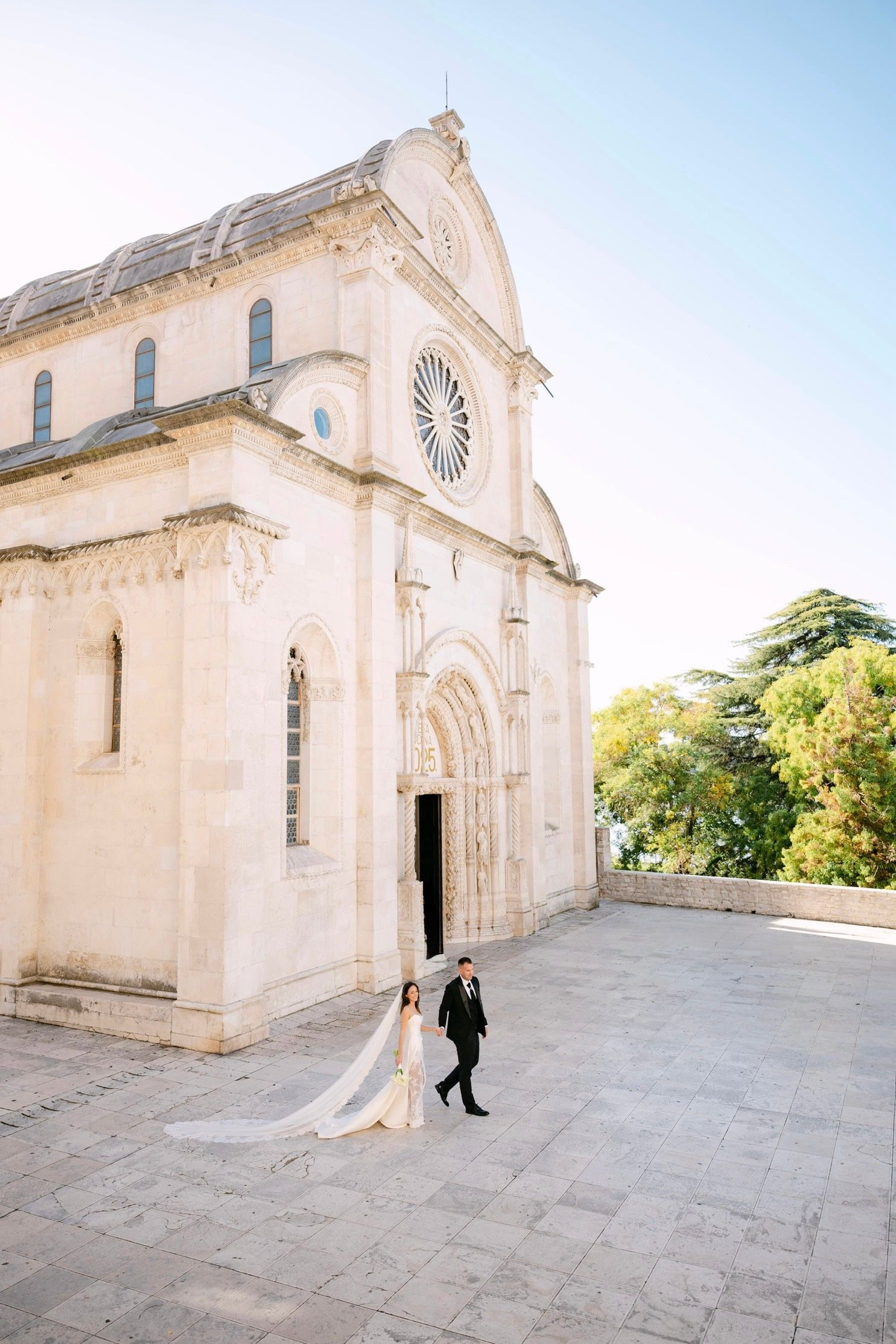 A couple stands in front of a majestic white stone cathedral in Croatia during their wedding photoshoot.
