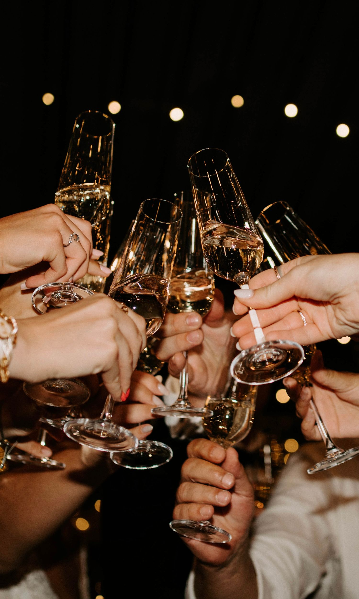 Multiple hands raising champagne flutes for celebratory toast against dark background.