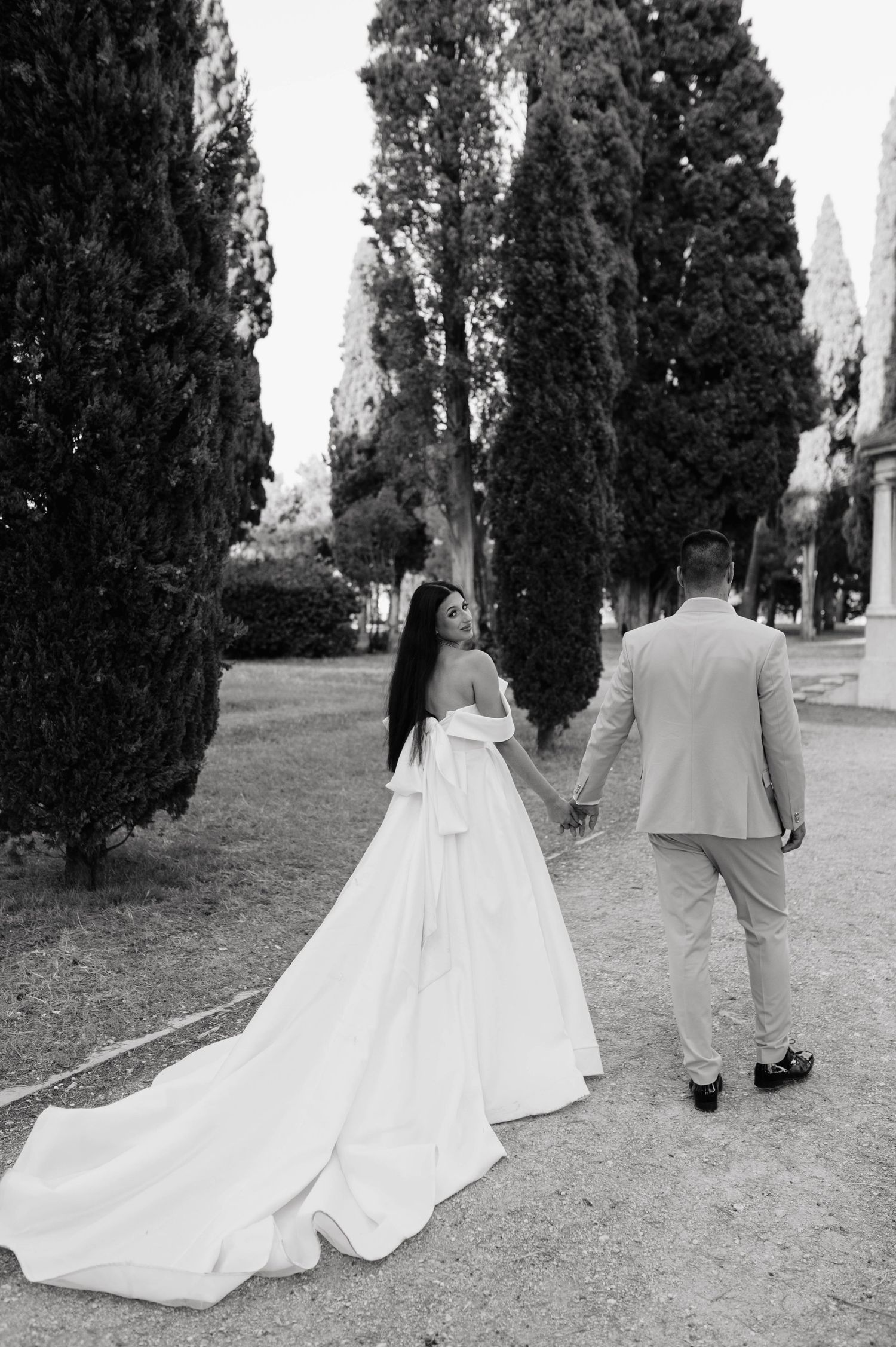 Black and white photo of a wedding couple walking among tall cypress trees.