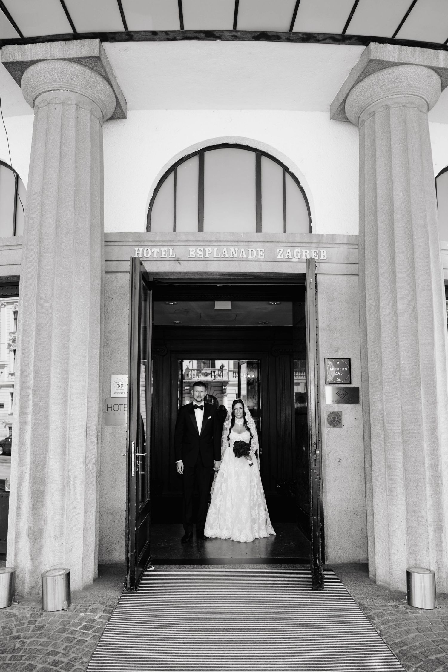Bride and groom exiting Hotel Esplanade Zagreb entrance in black and white wedding photo.