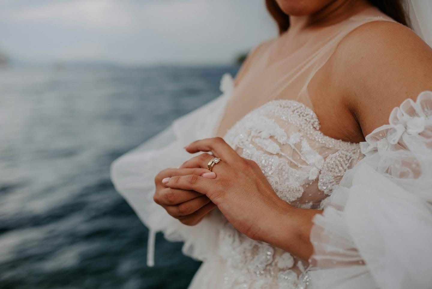 Close-up of a wedding ring and lace dress detail against an ocean backdrop.