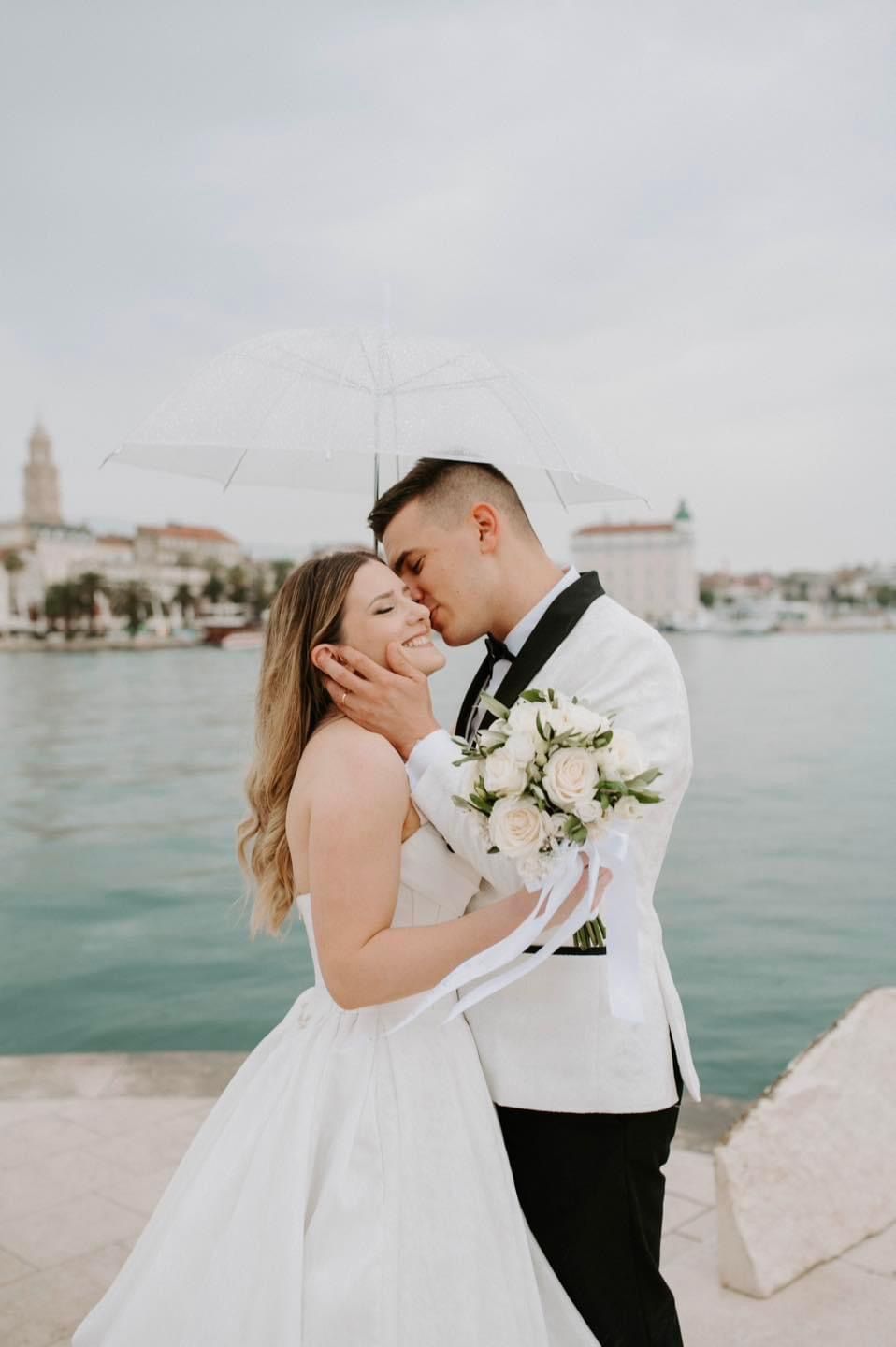 A romantic waterfront wedding portrait with a couple embracing near a coastal village.