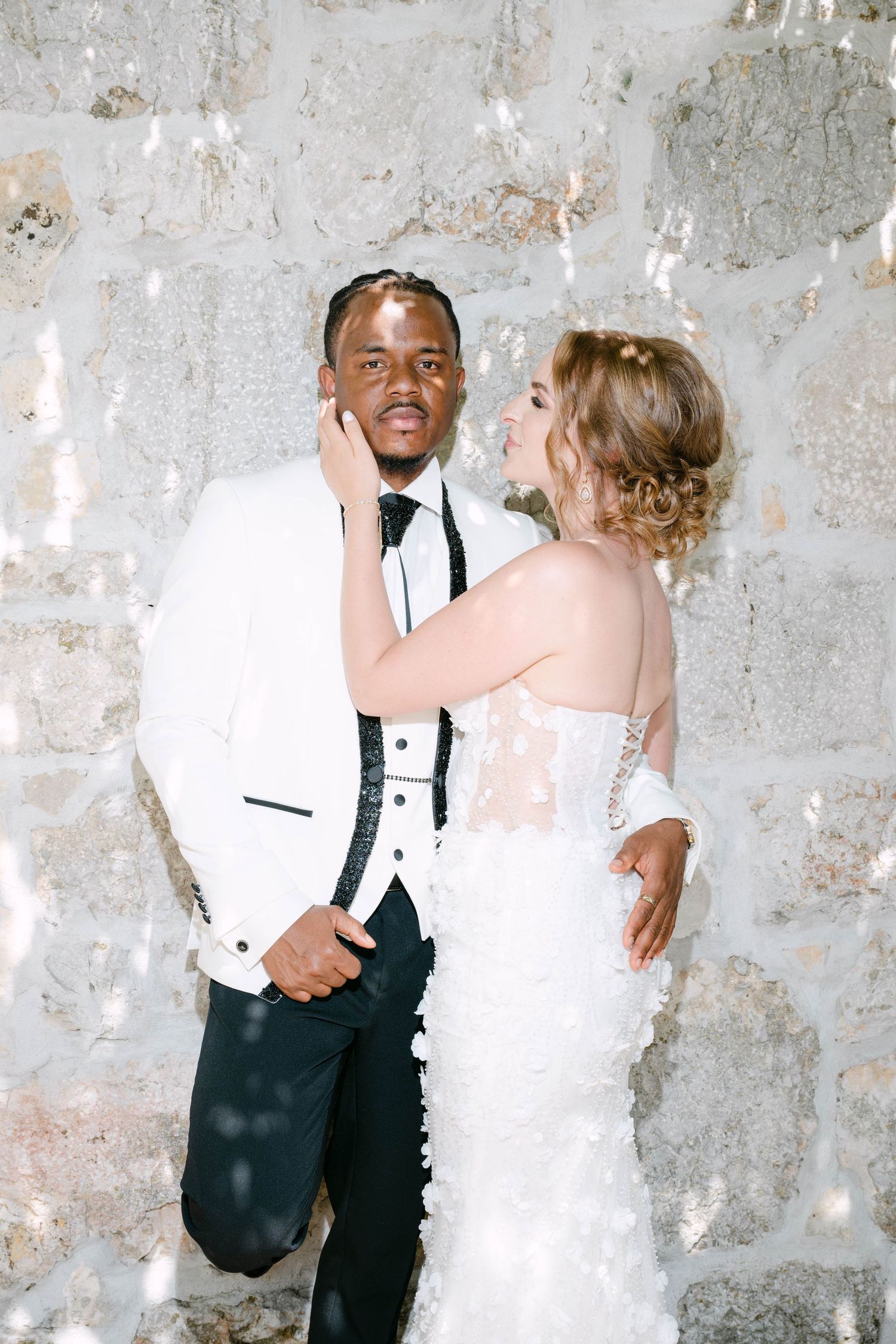 A happy couple shares a romantic dance together against a textured concrete wall at their wedding celebration.