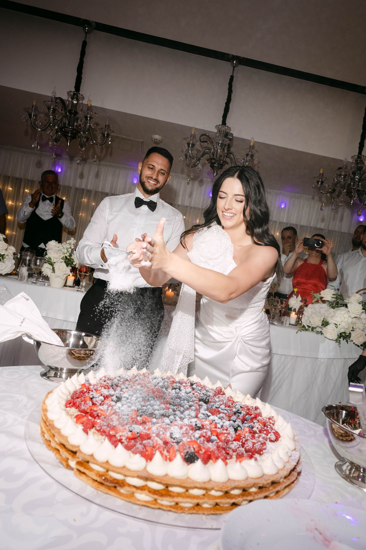 A sequence of photos showing a couple playfully cutting and smashing a large layered cream cake at their wedding reception.