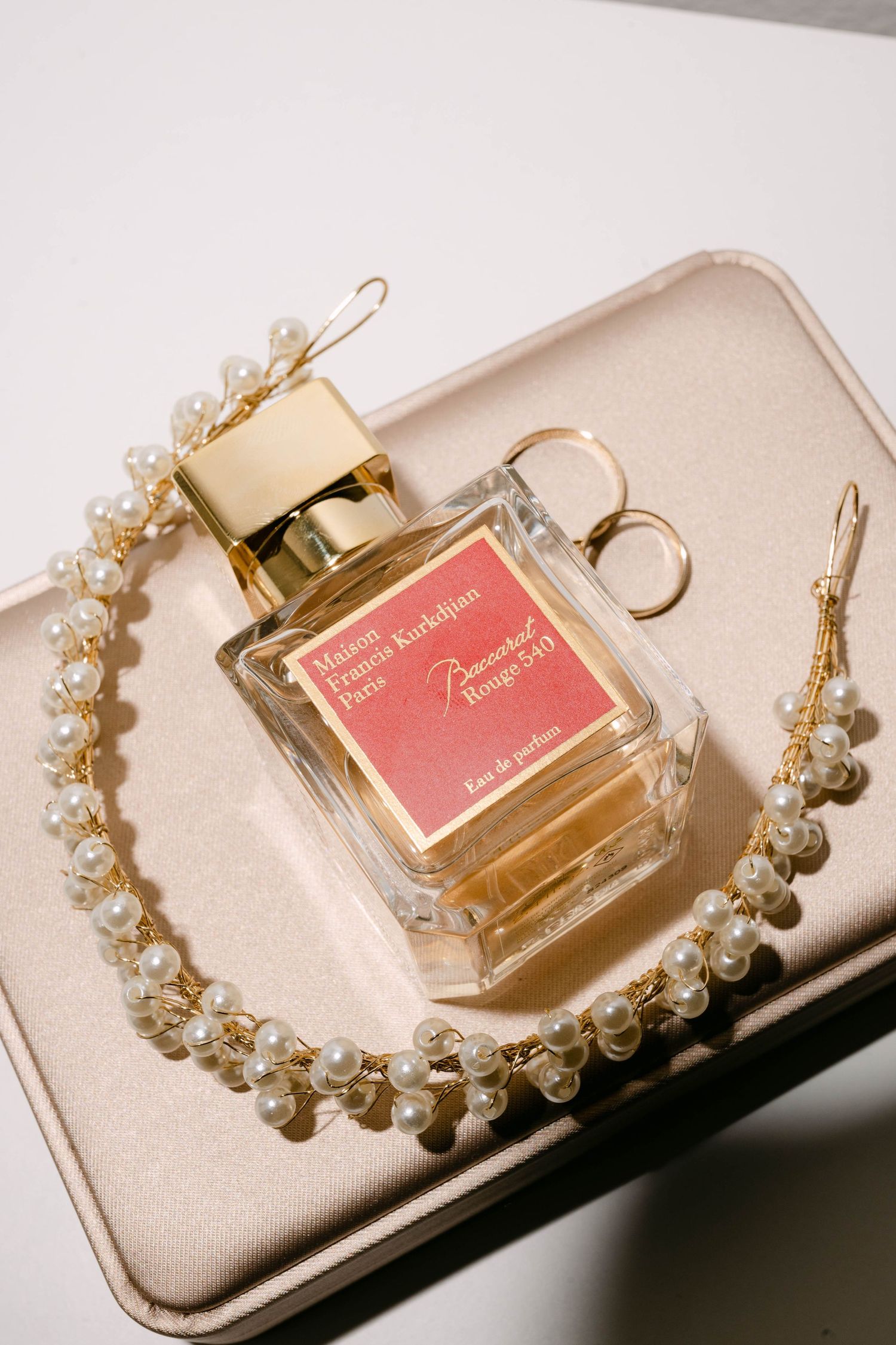 A pink perfume bottle sits elegantly beside a delicate pearl bracelet on a beige surface in soft lighting.