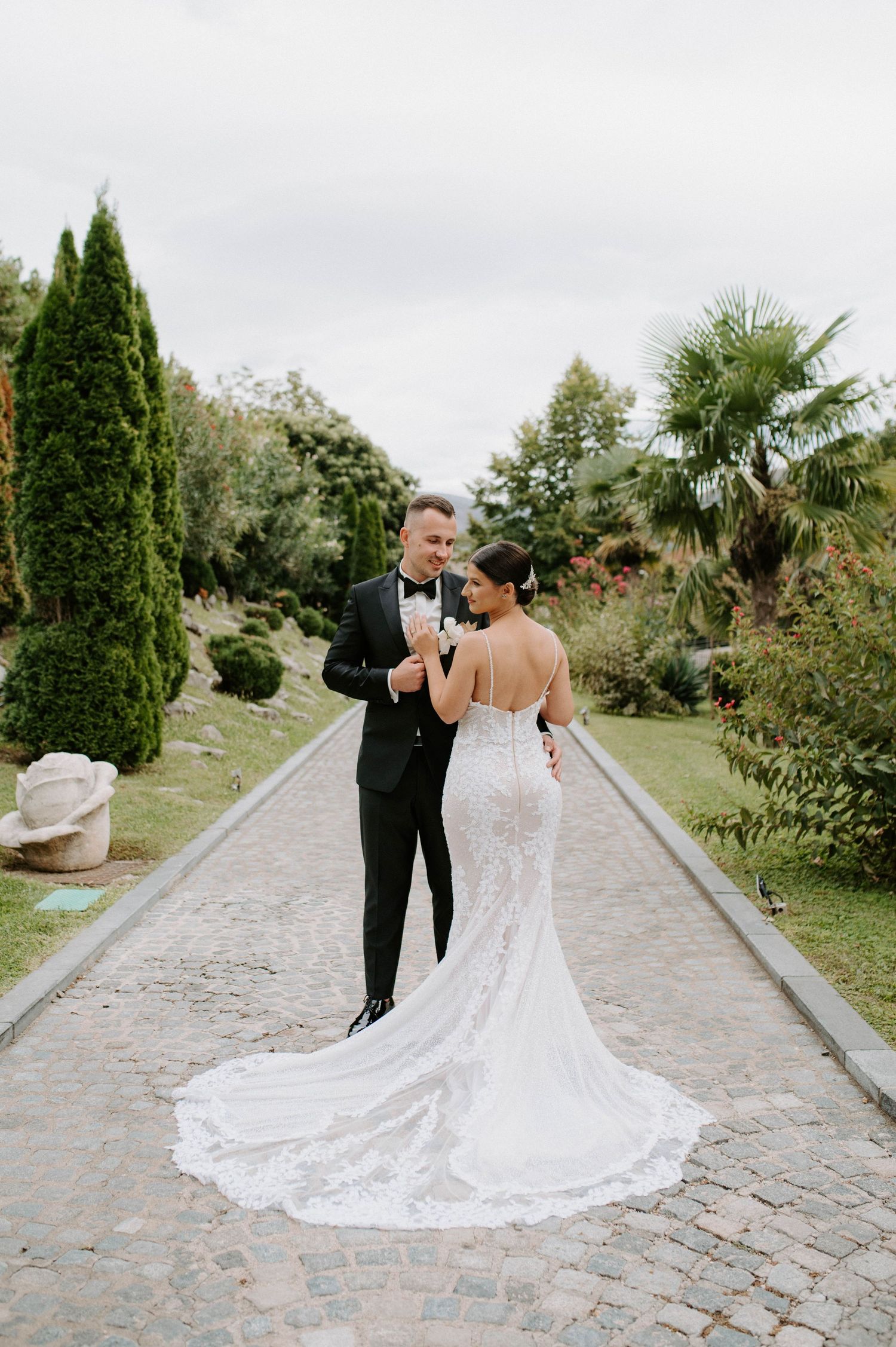 Newlyweds walking down garden path with stunning lace wedding dress train trailing behind.