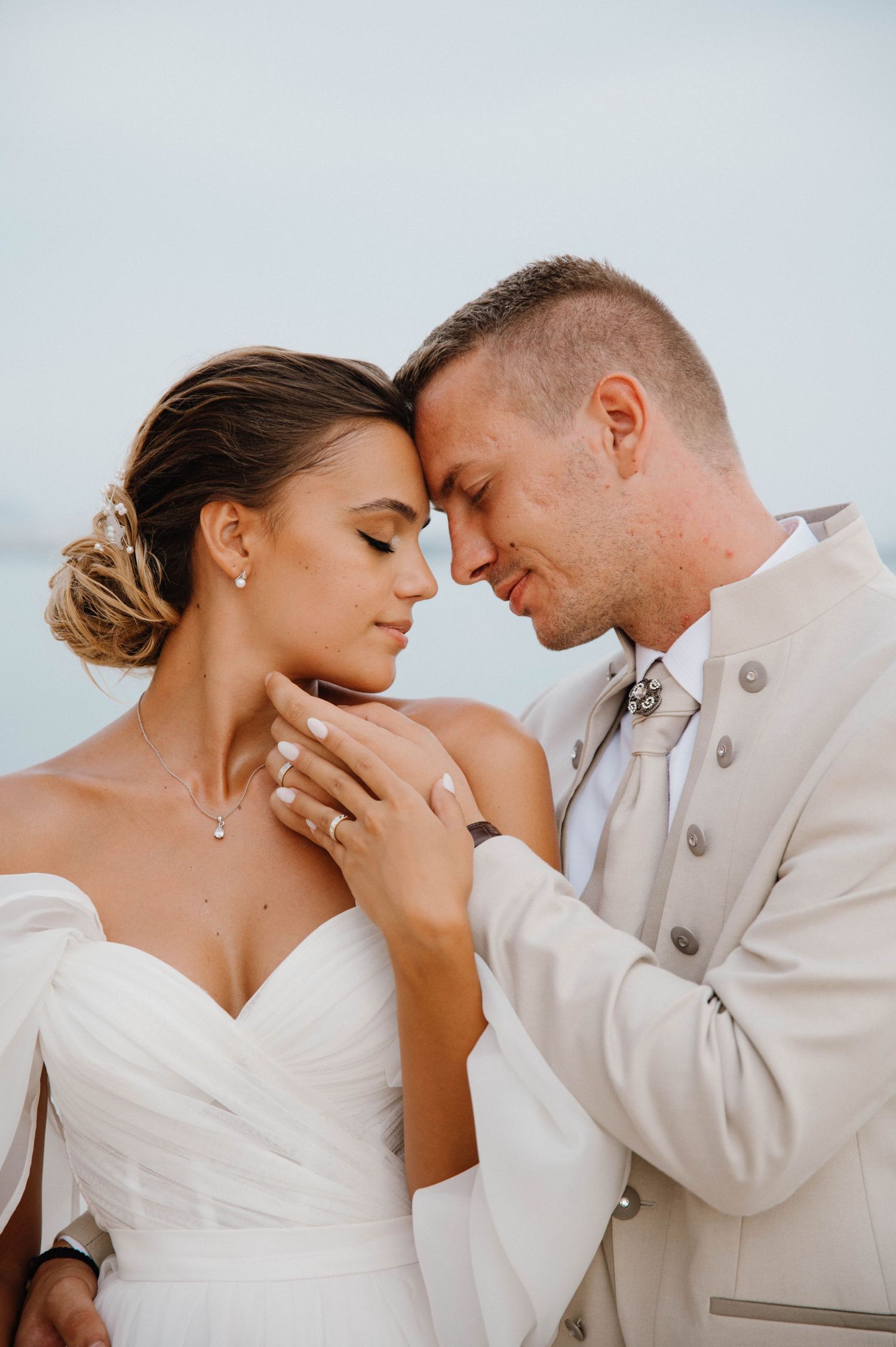A romantic wedding portrait showing a couple embracing in soft sunlight by the ocean.